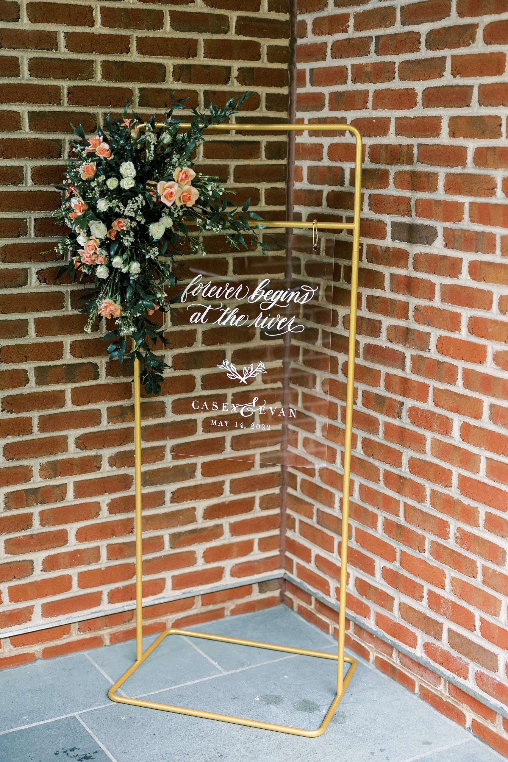 acrylic sign hangs on gold piping outside ceremony 