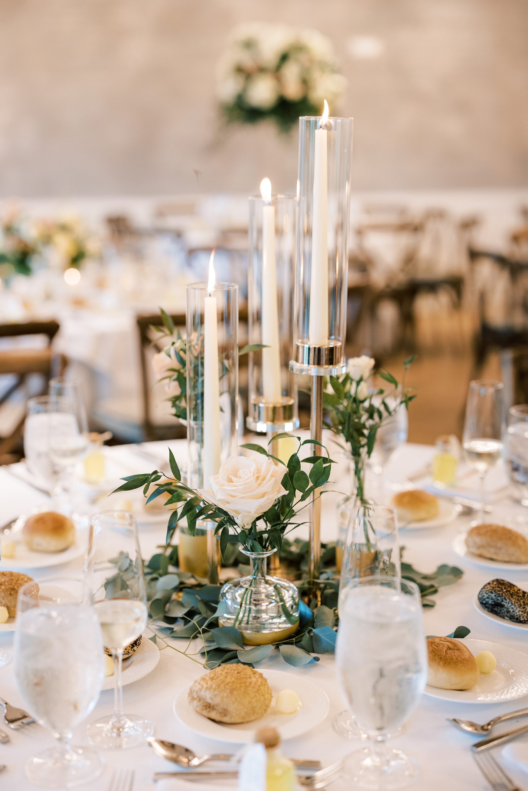 centerpieces with greenery and tall thin white candles 