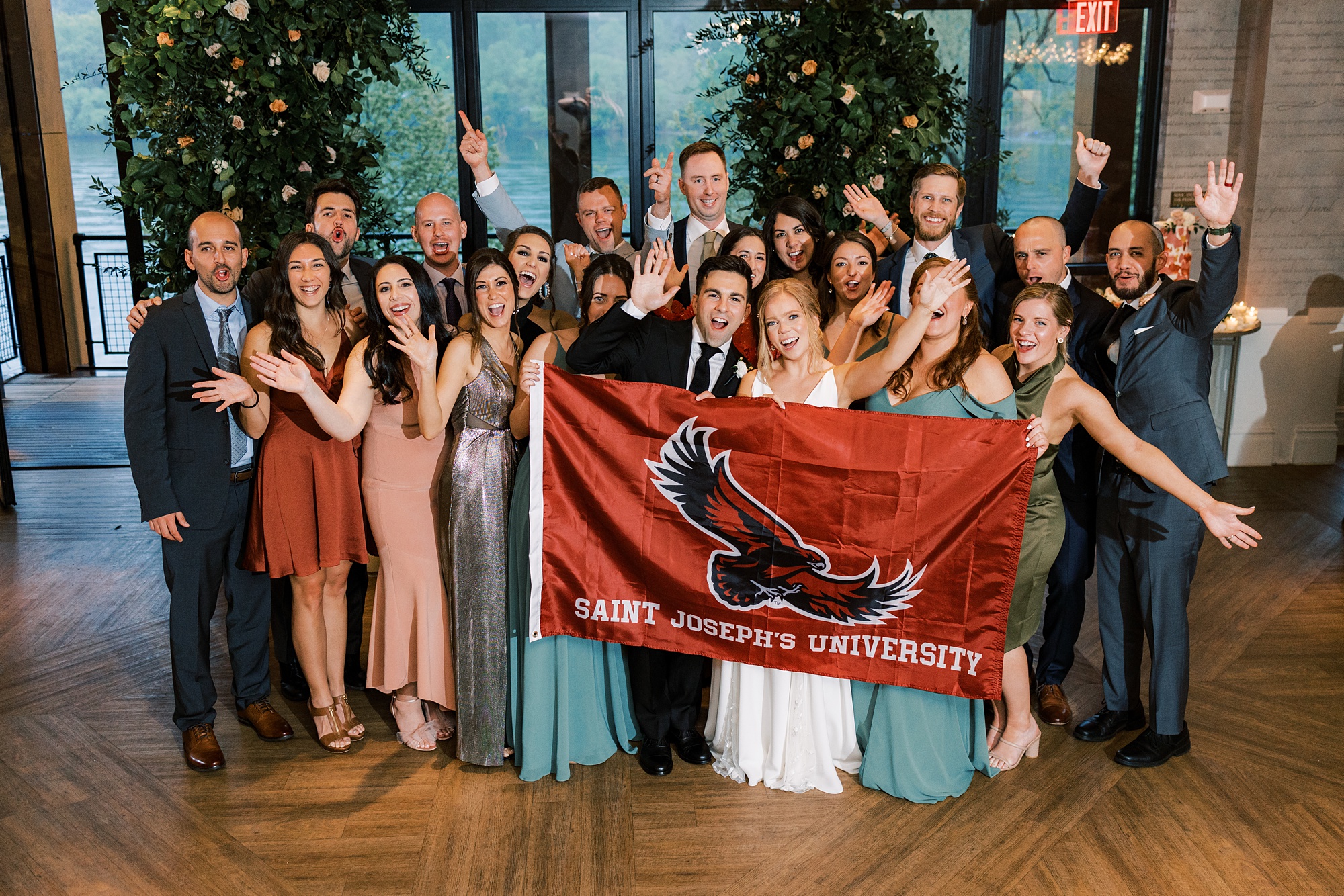 bride and groom pose with college friends and St. Joseph's University flag