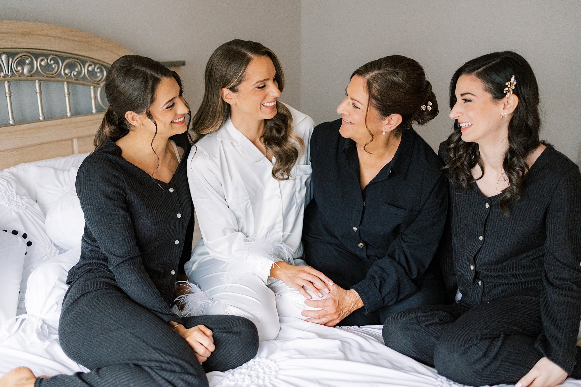 bride sits with bridesmaids and mother in matching black pajamas in childhood home 