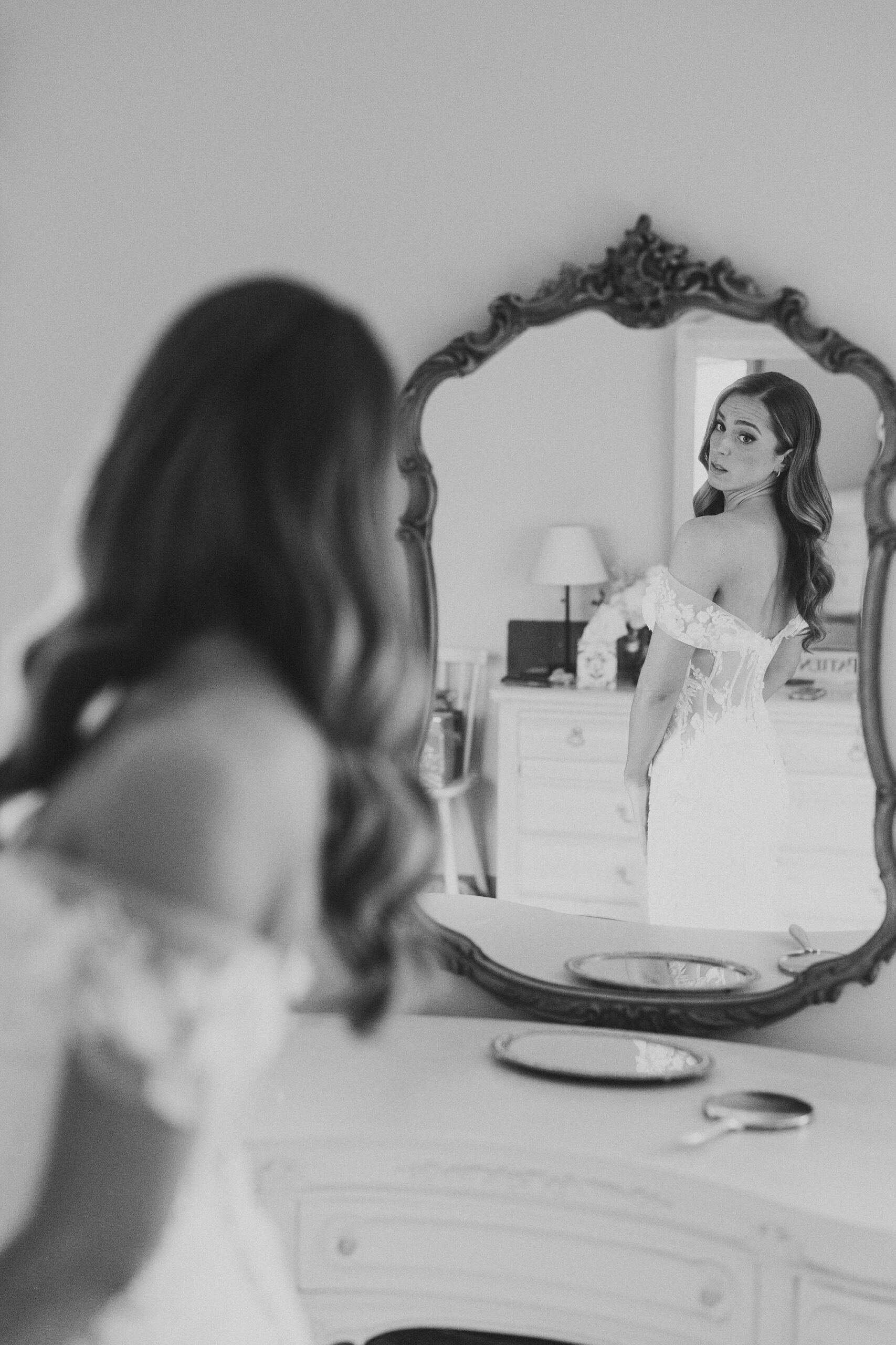 bride looks at self in mirror above grandmother's vanity in NJ