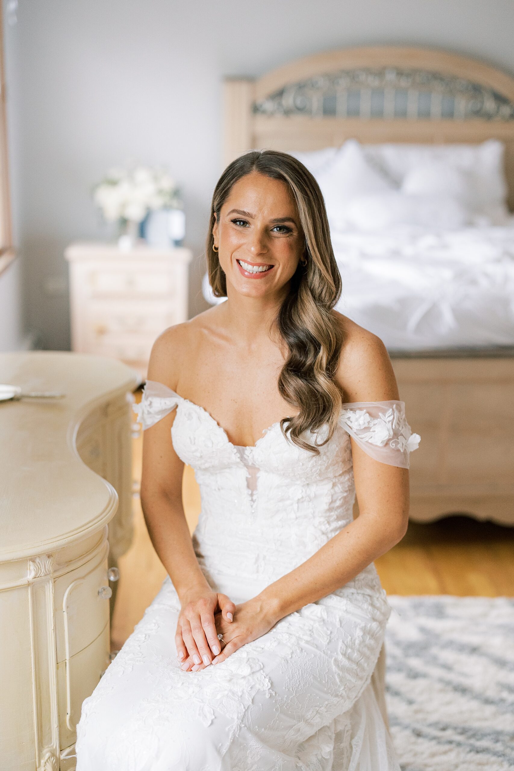 blonde bride sits in wedding gown with off-the-shoulder gown 