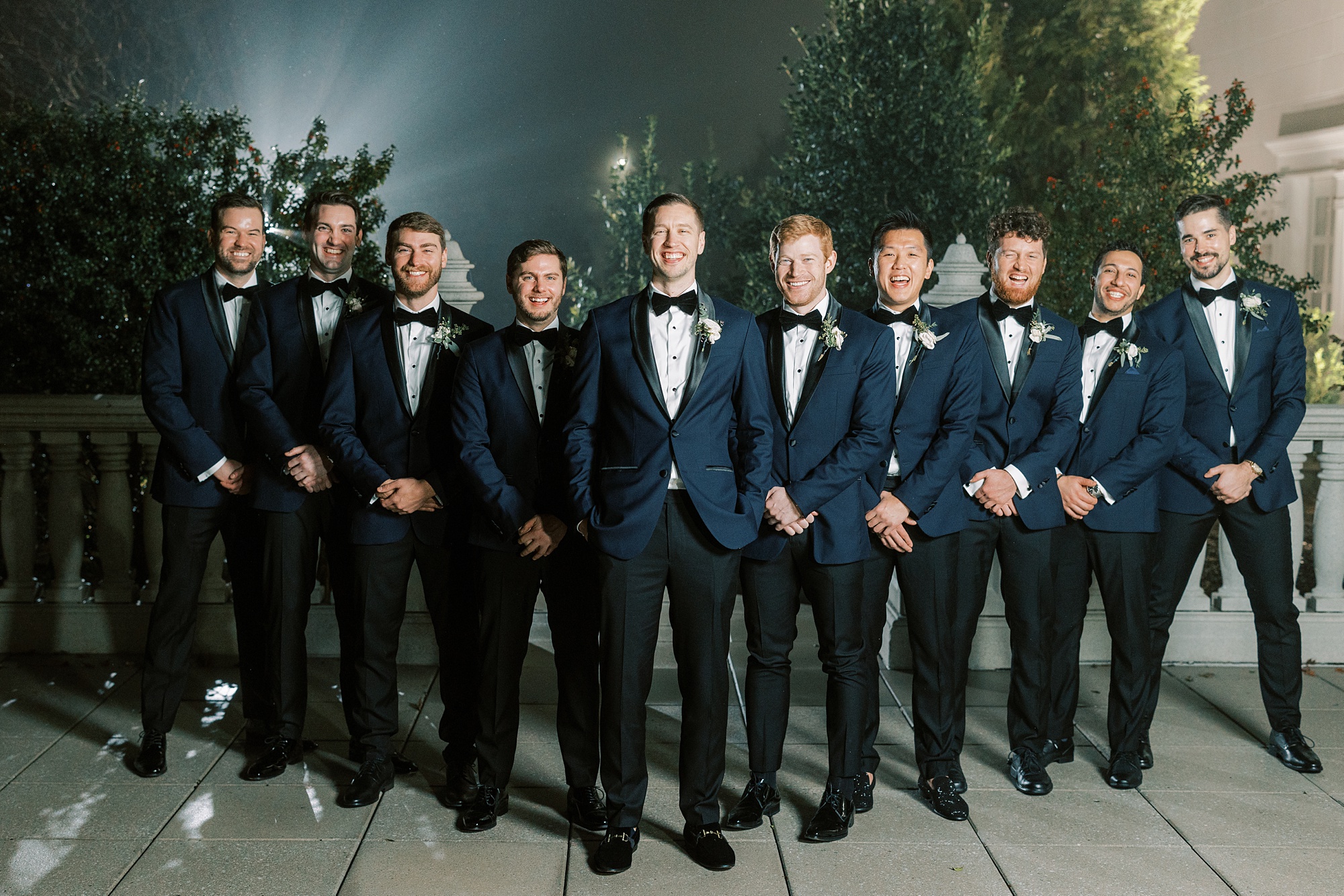 groom stands with groomsmen behind him in blue suits 