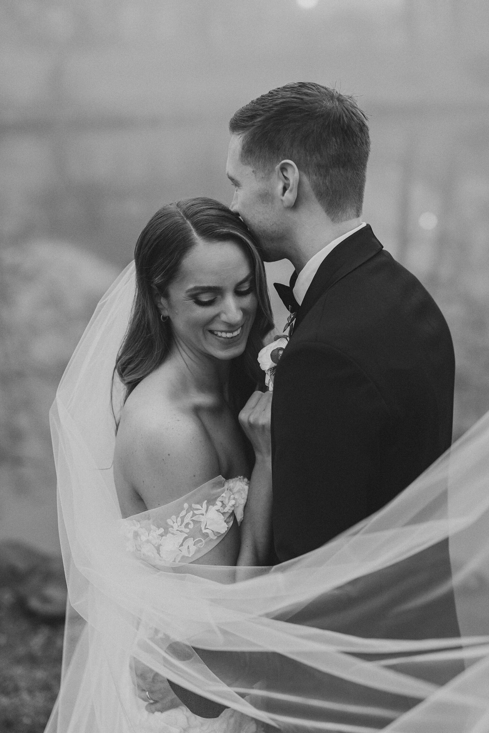 black and white portrait of bride and groom hugging with veil around them 