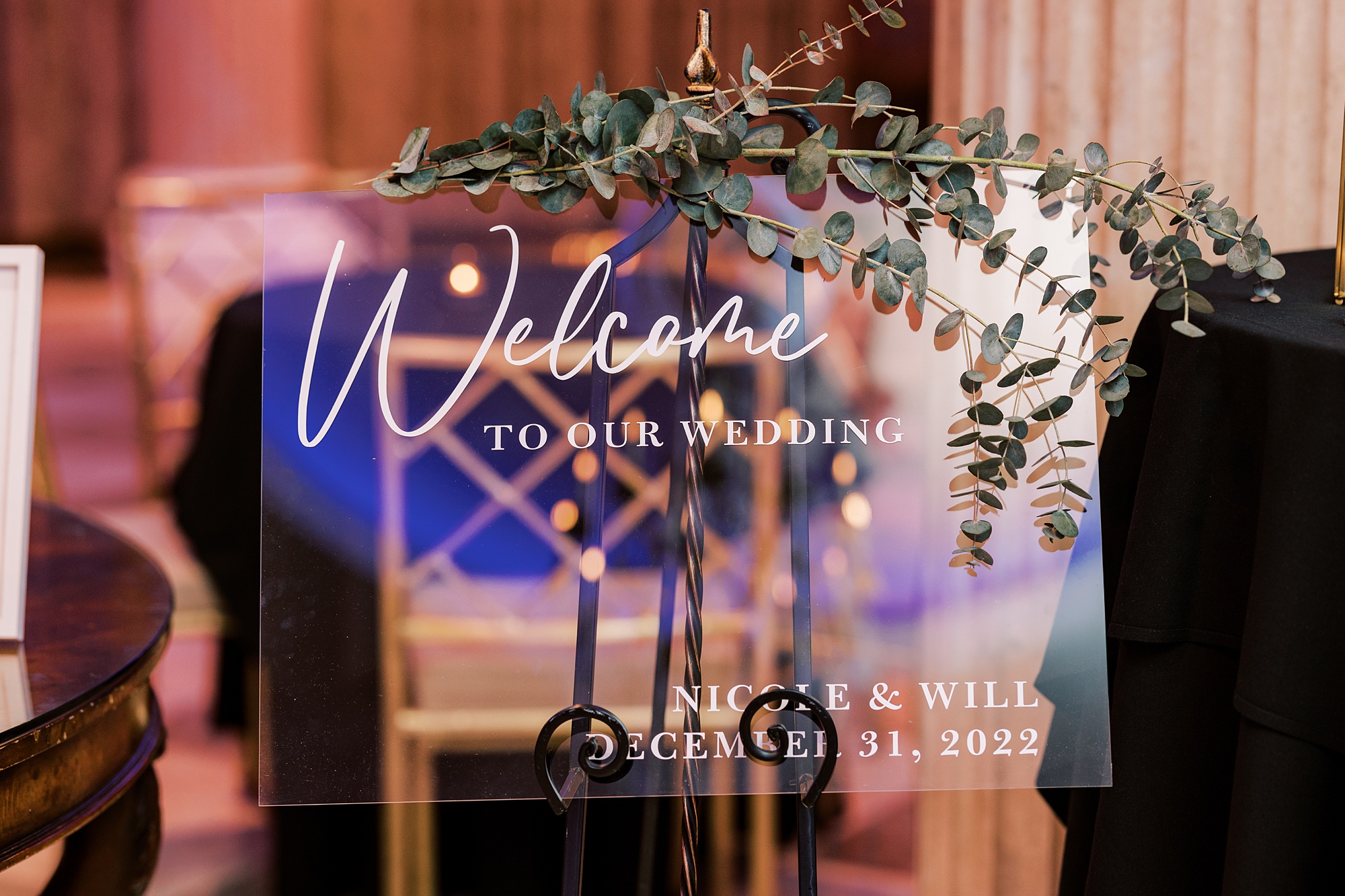 welcome sign on acrylic board with greenery draped on top 