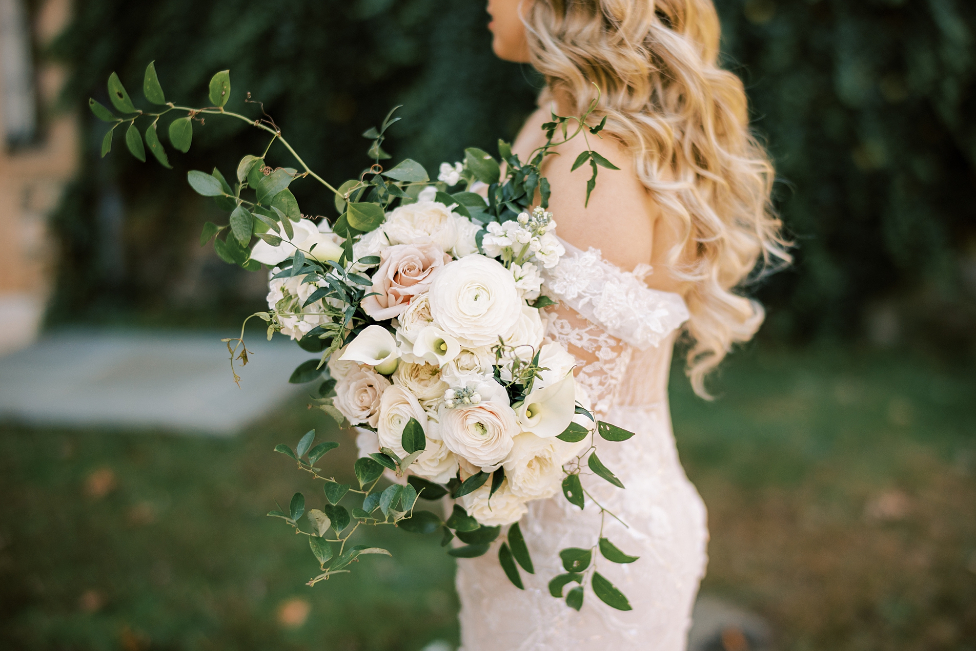 bride holds bouquet of ivory and pale pink roses in arms 