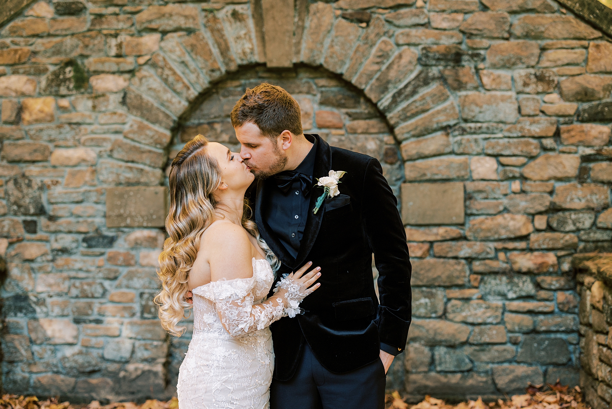 bride and groom kiss by stone wall at Parque Ridley Creek