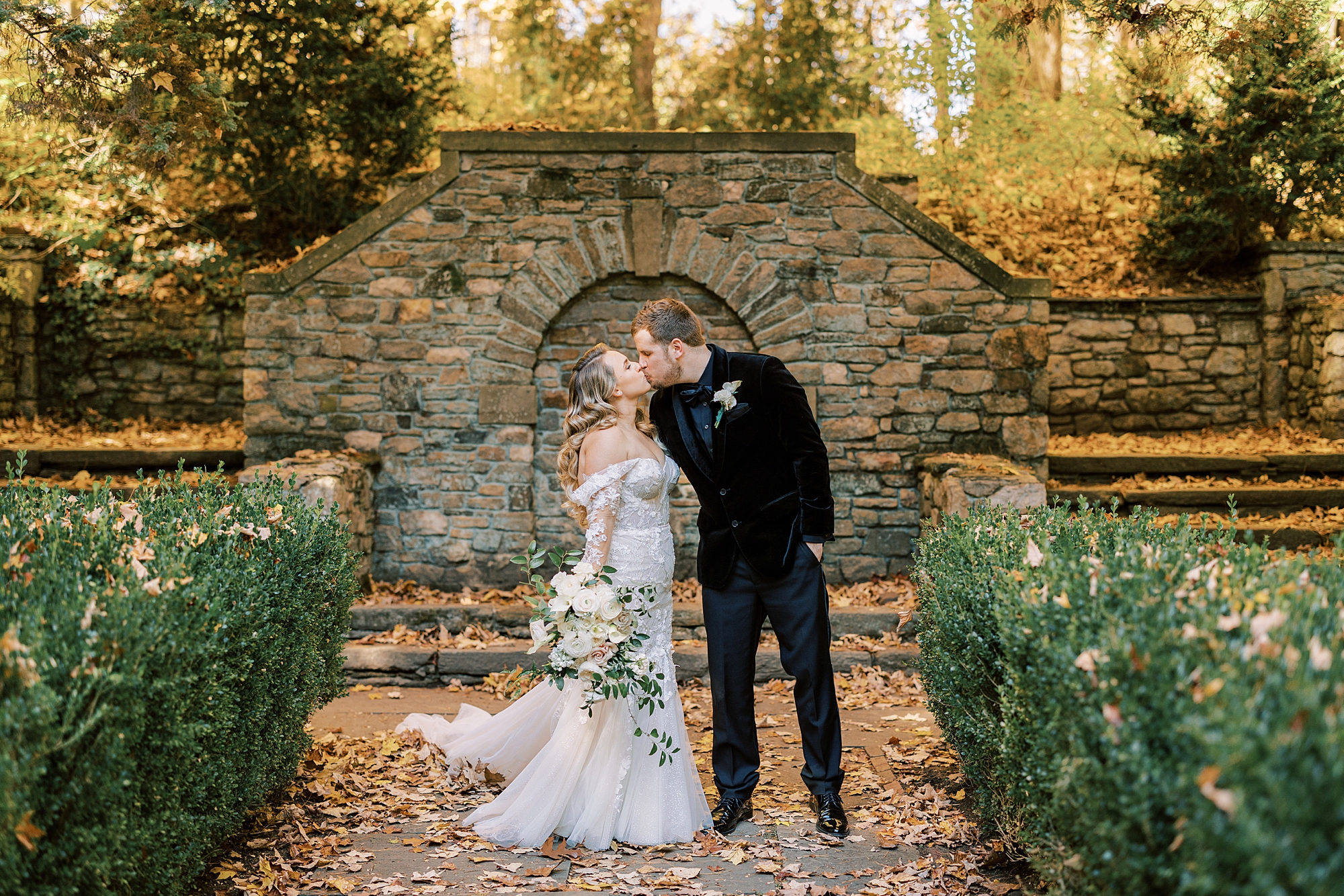 newlyweds kiss by stone wall in gardens at Parque Ridley Creek