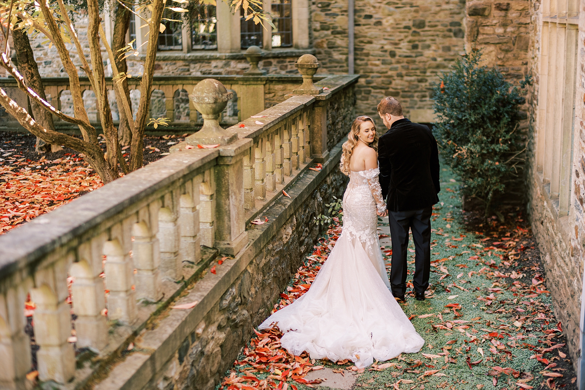 groom leans to whisper in bride's ear as they walk down stone walkway 