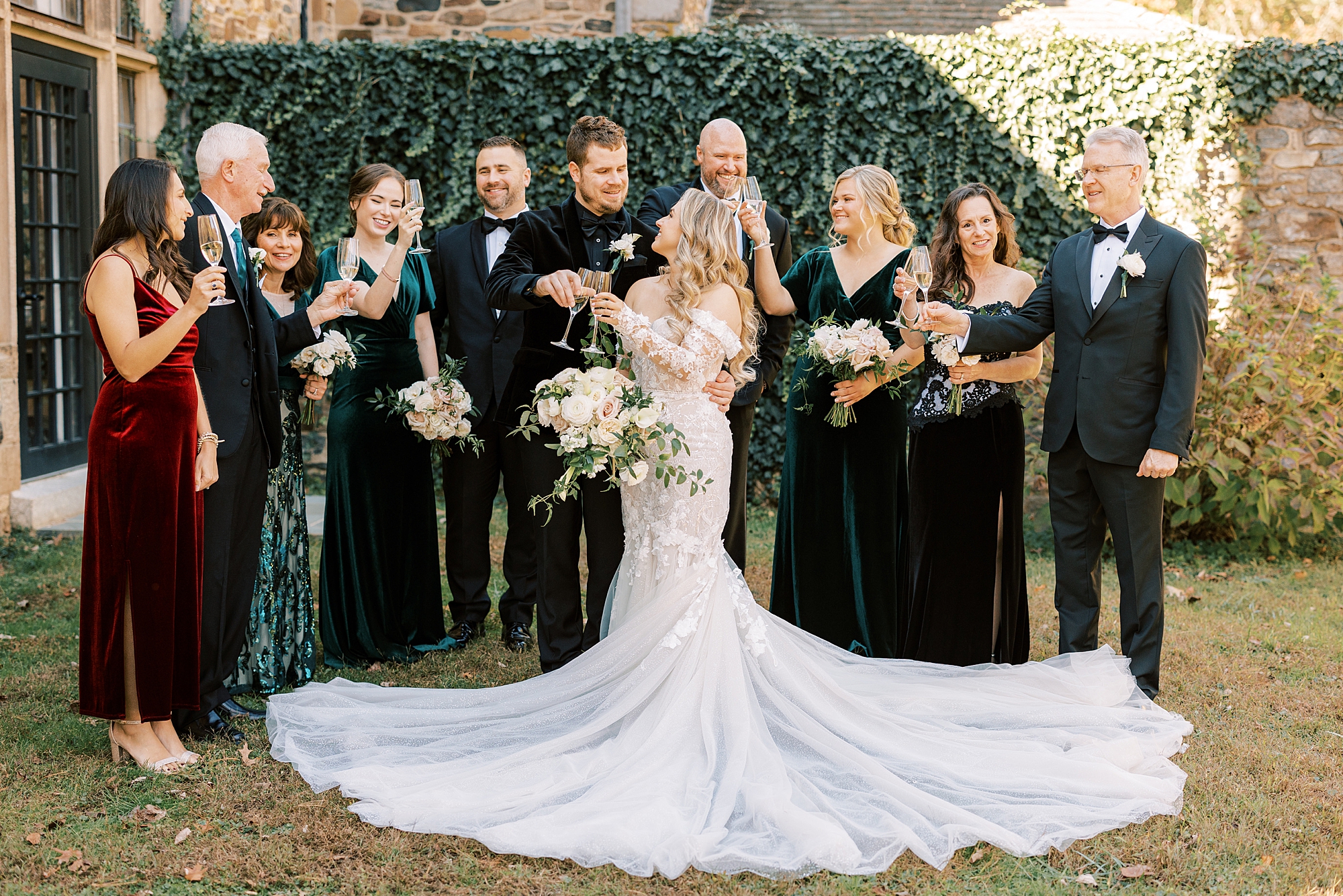 bride and groom smile with family around them in front of ivy wall 