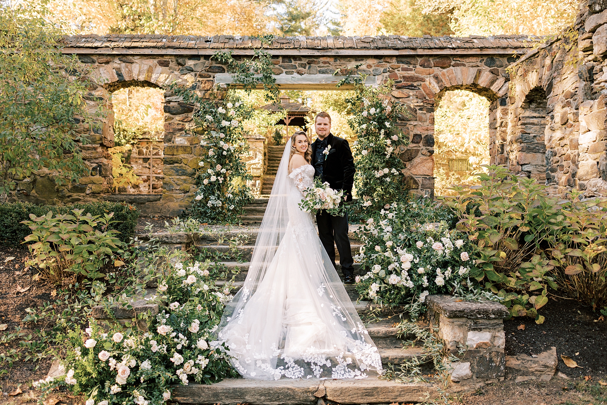 bride and groom pose on stone steps with white and green floral arrangements 