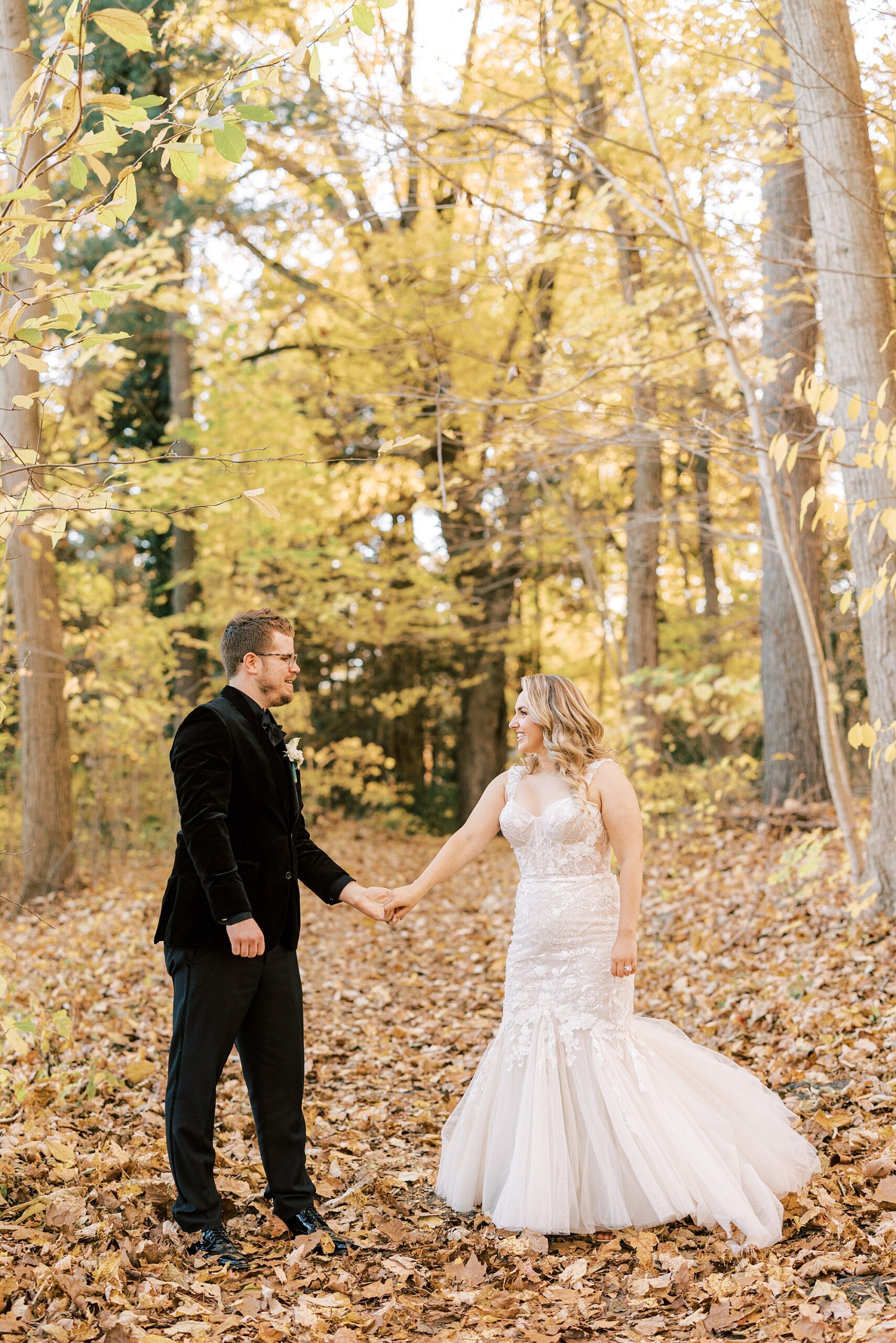 bride and groom hold hands walking through fallen leaves 