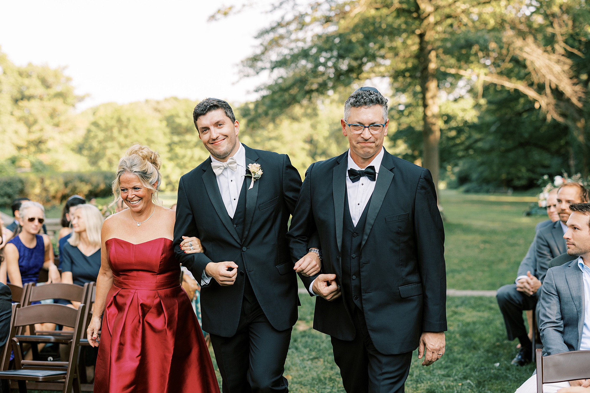 groom walks down aisle with parents for wedding ceremony on lawn at Curtis Arboretum