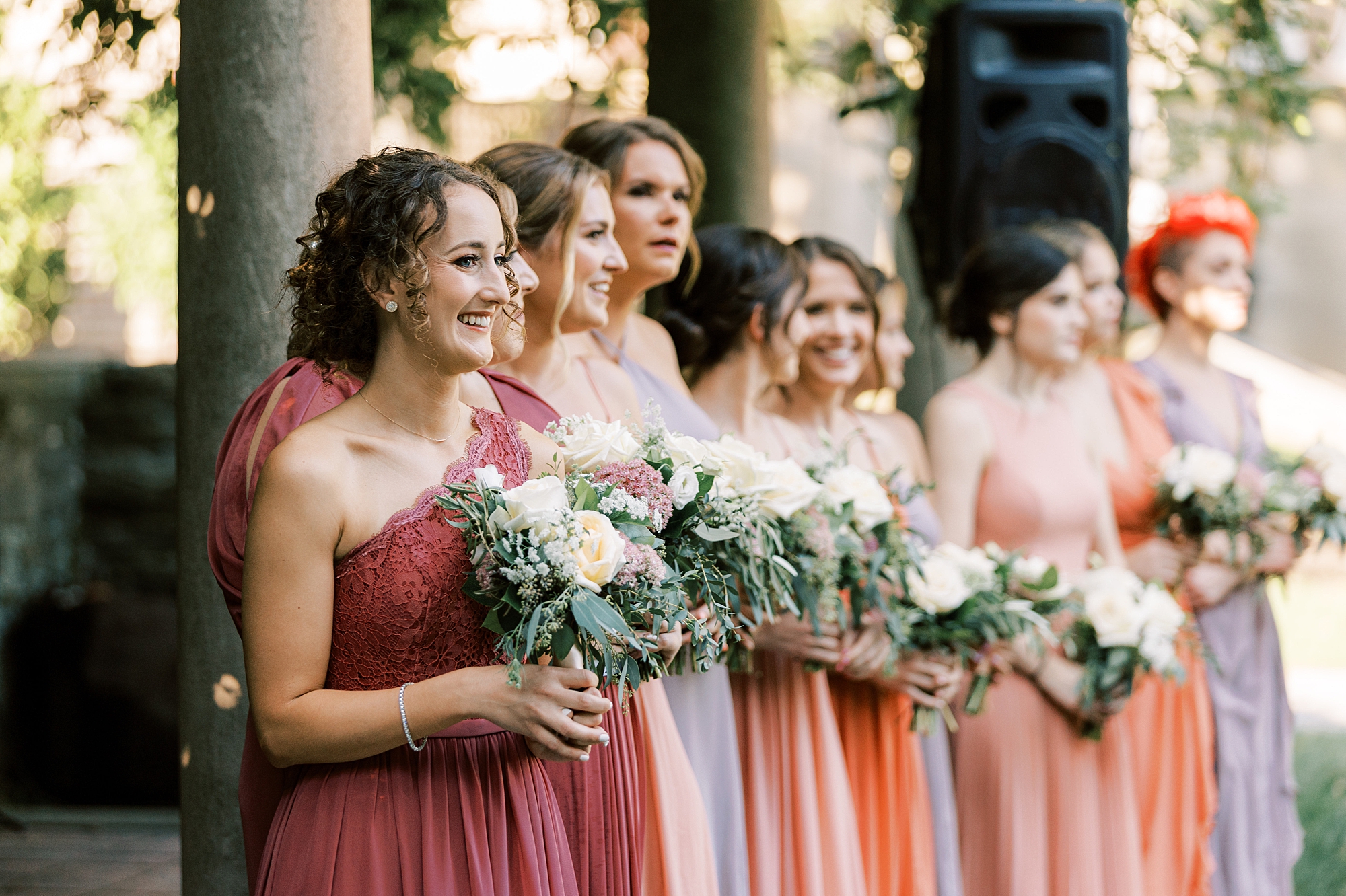 bridesmaids in mismatched red and pink gowns at Curtis Arboretum wedding ceremony on lawn