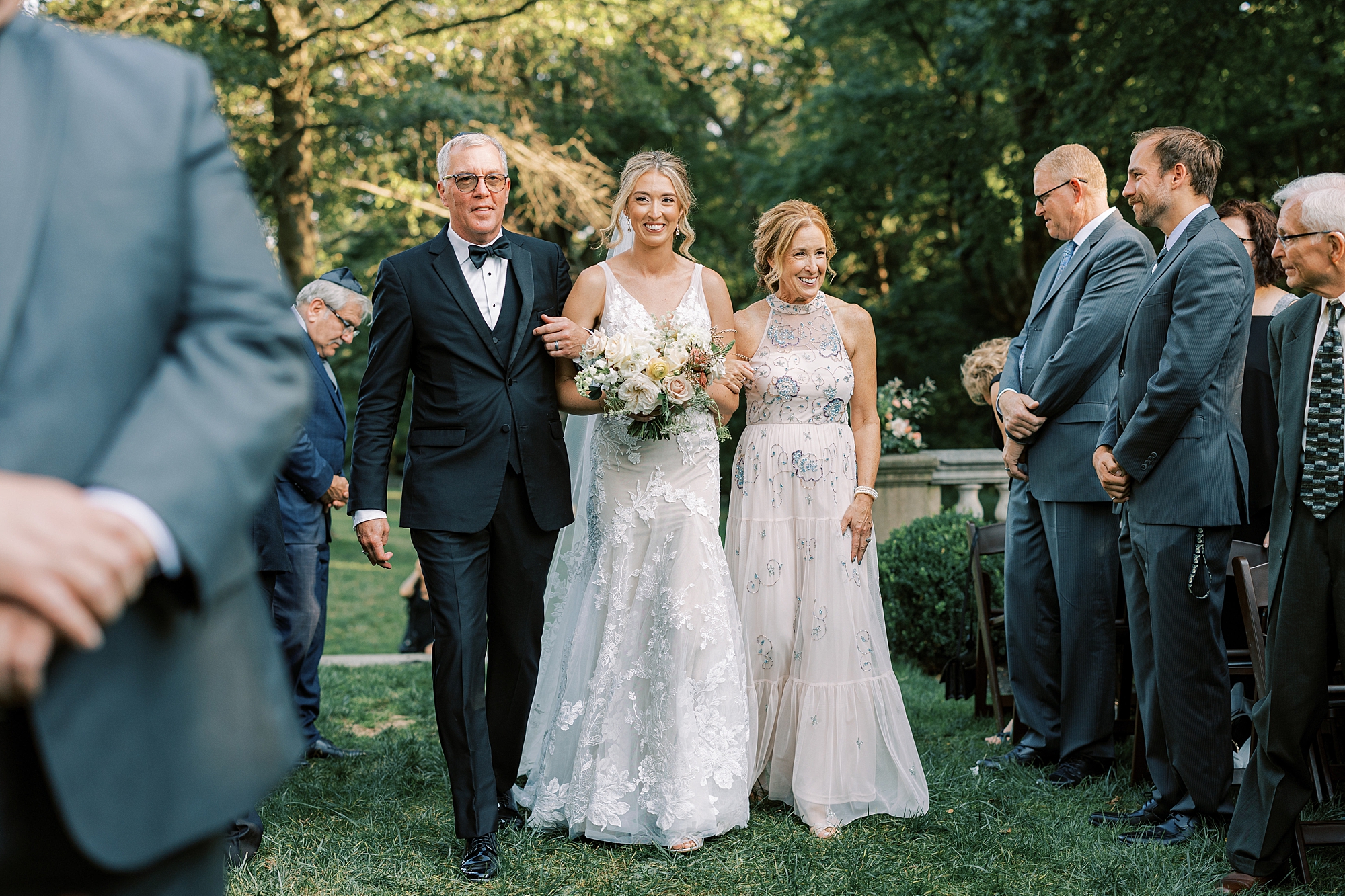 bride walks down aisle during Curtis Arboretum wedding ceremony on lawn