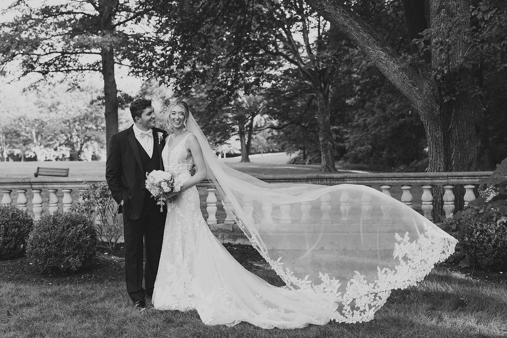 black and white portrait of bride and groom hugging with veil floating behind them