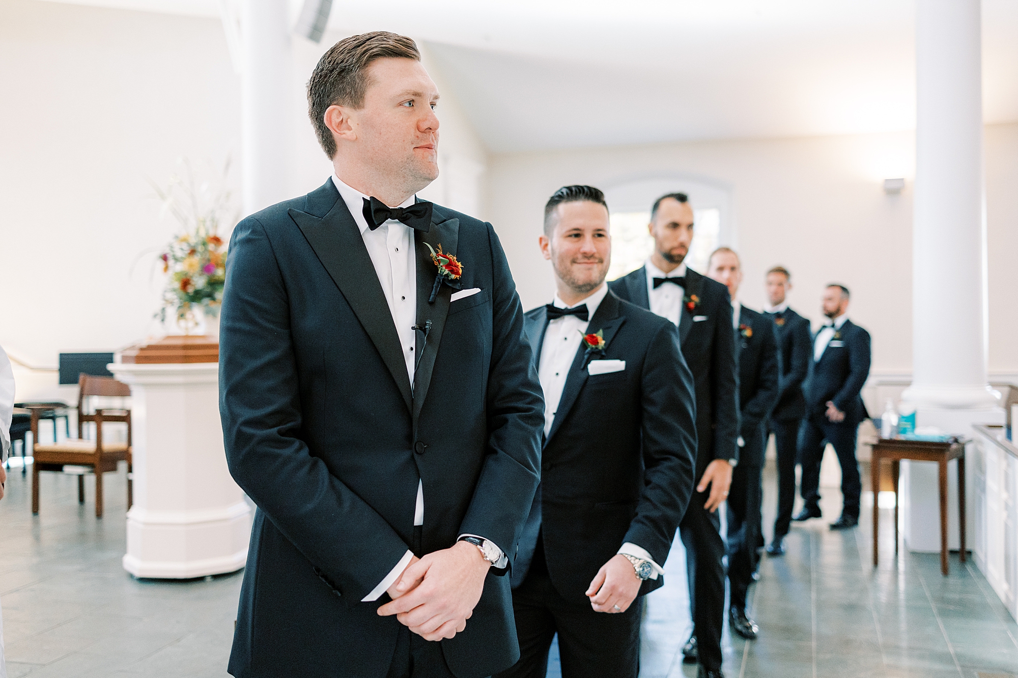 groom stands at front of church in black suit with groomsmen at St. David’s Episcopal Church 