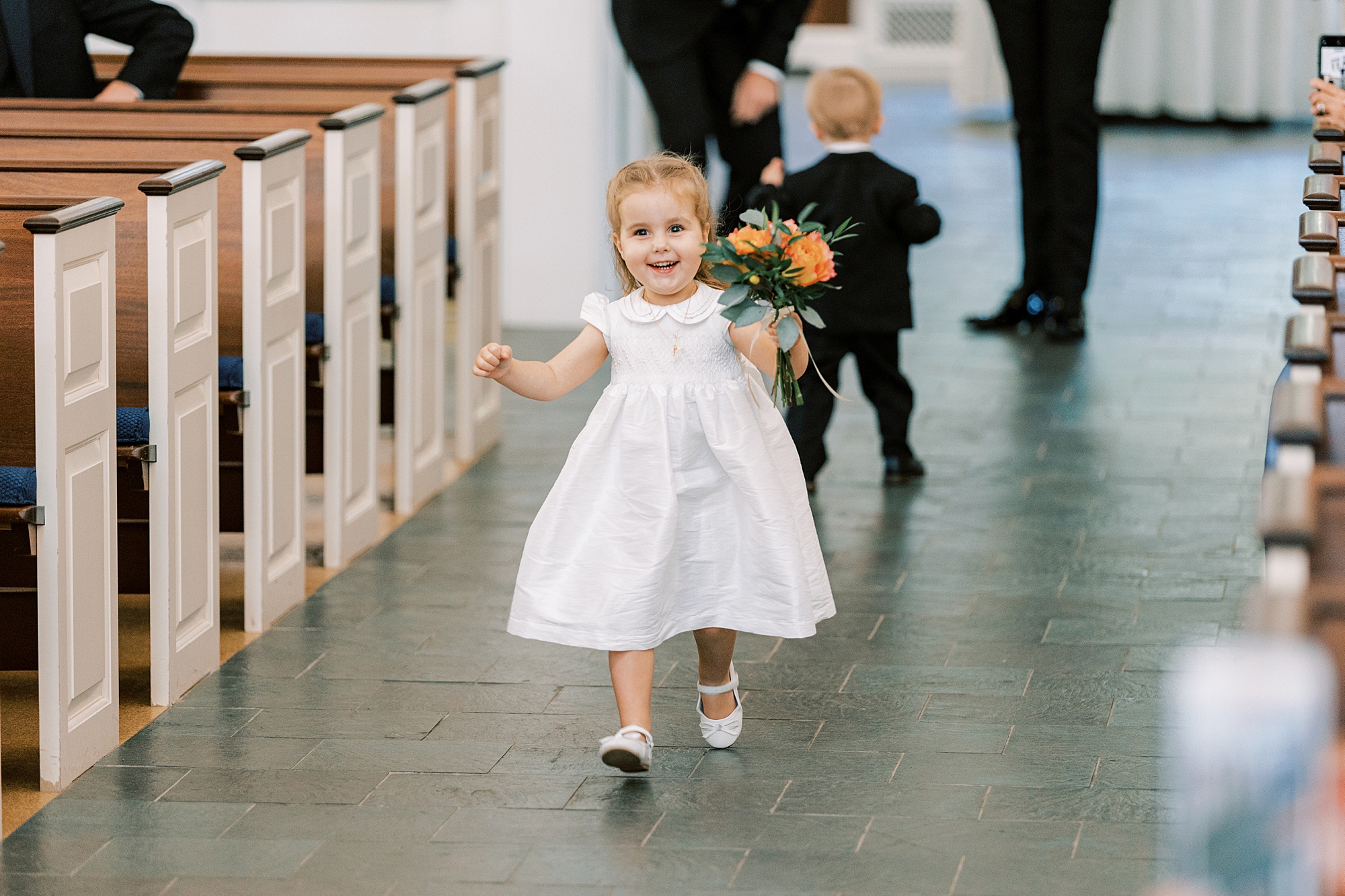 flower girl in white dress walks down aisle for church ceremony 