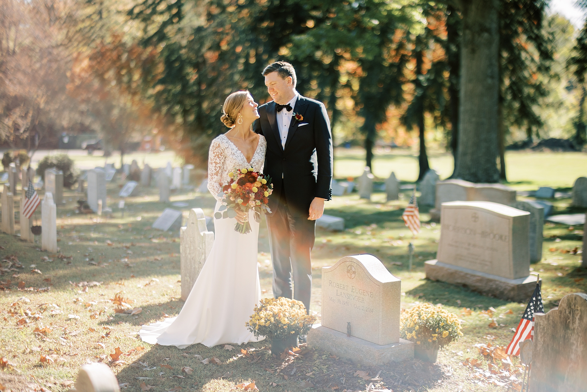 newlyweds stand by father's headstone in cemetery at St. David’s Episcopal Church 