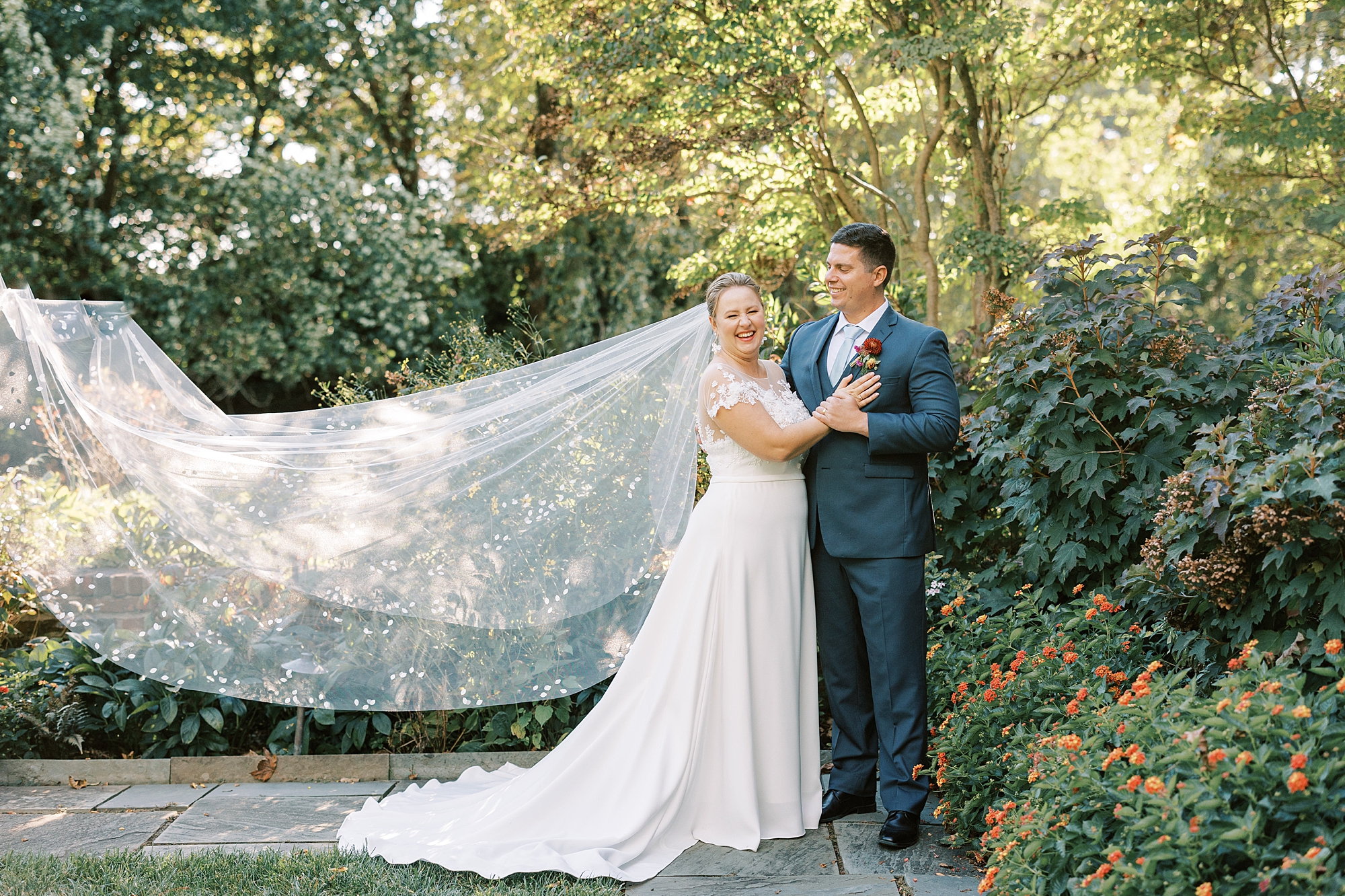 bride and groom hug in garden at Greenville Country Club with veil floating behind bride 