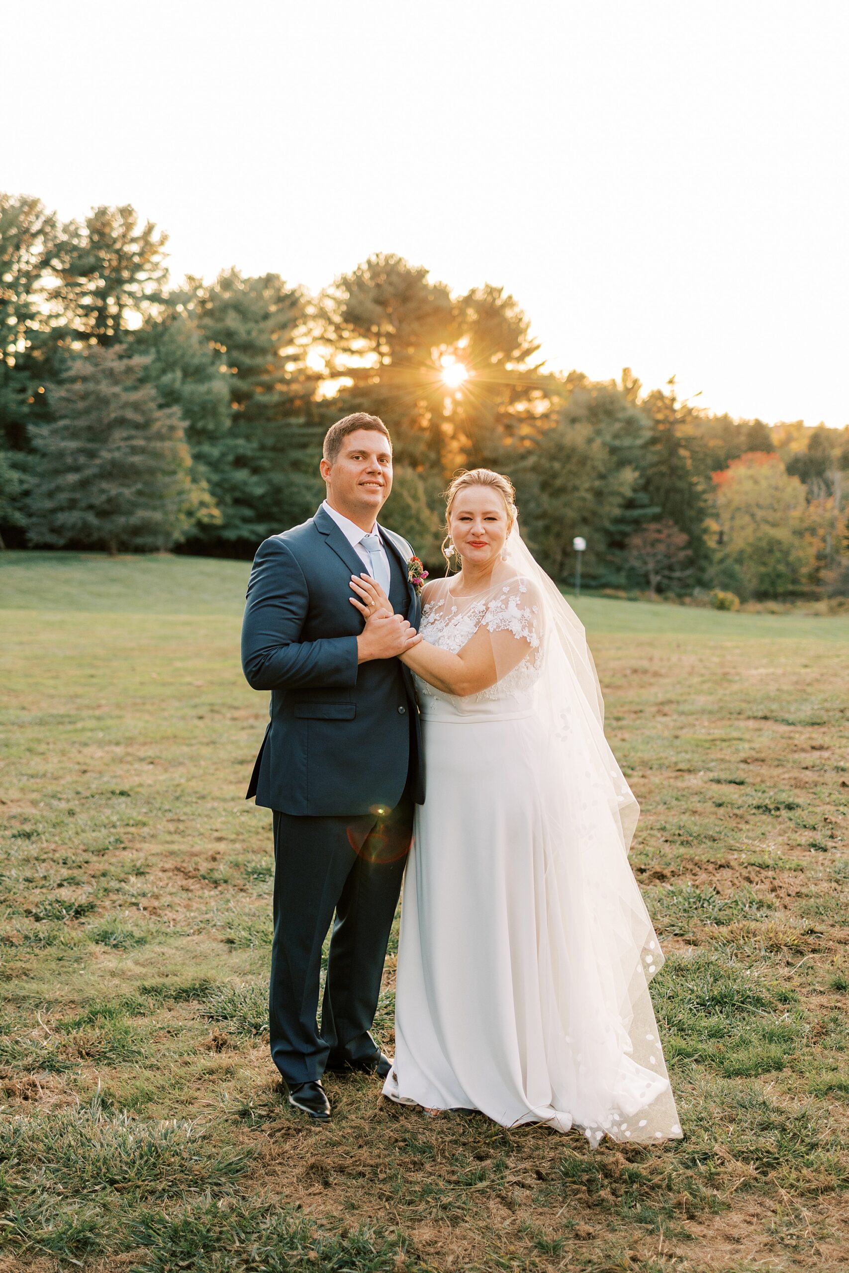 newlyweds smile together on lawn at sunset
