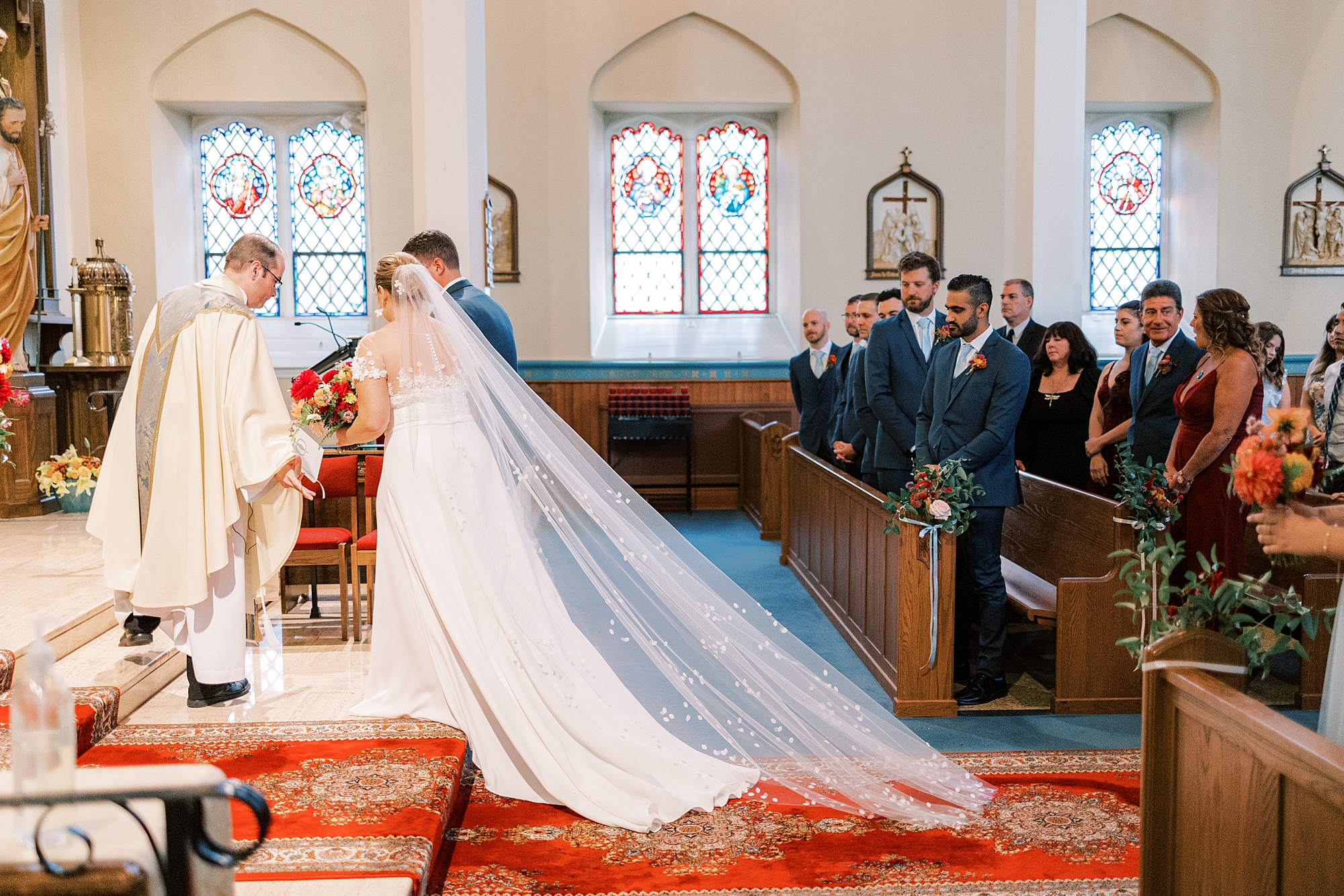 bride walks down aisle with veil behind her at St. Ann’s Roman Catholic Church