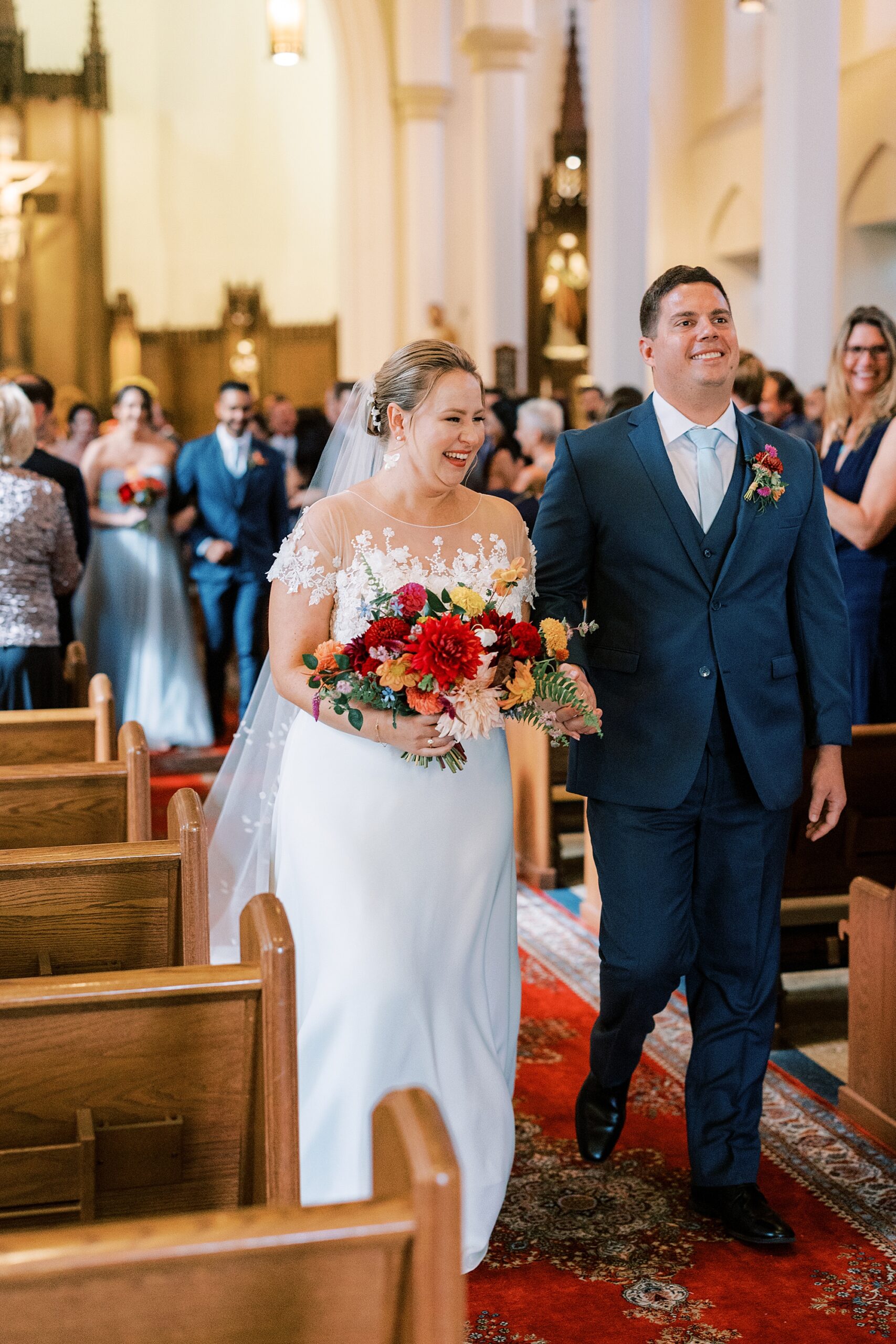 bride and groom hold hands walking up aisle at St. Ann’s Roman Catholic Church