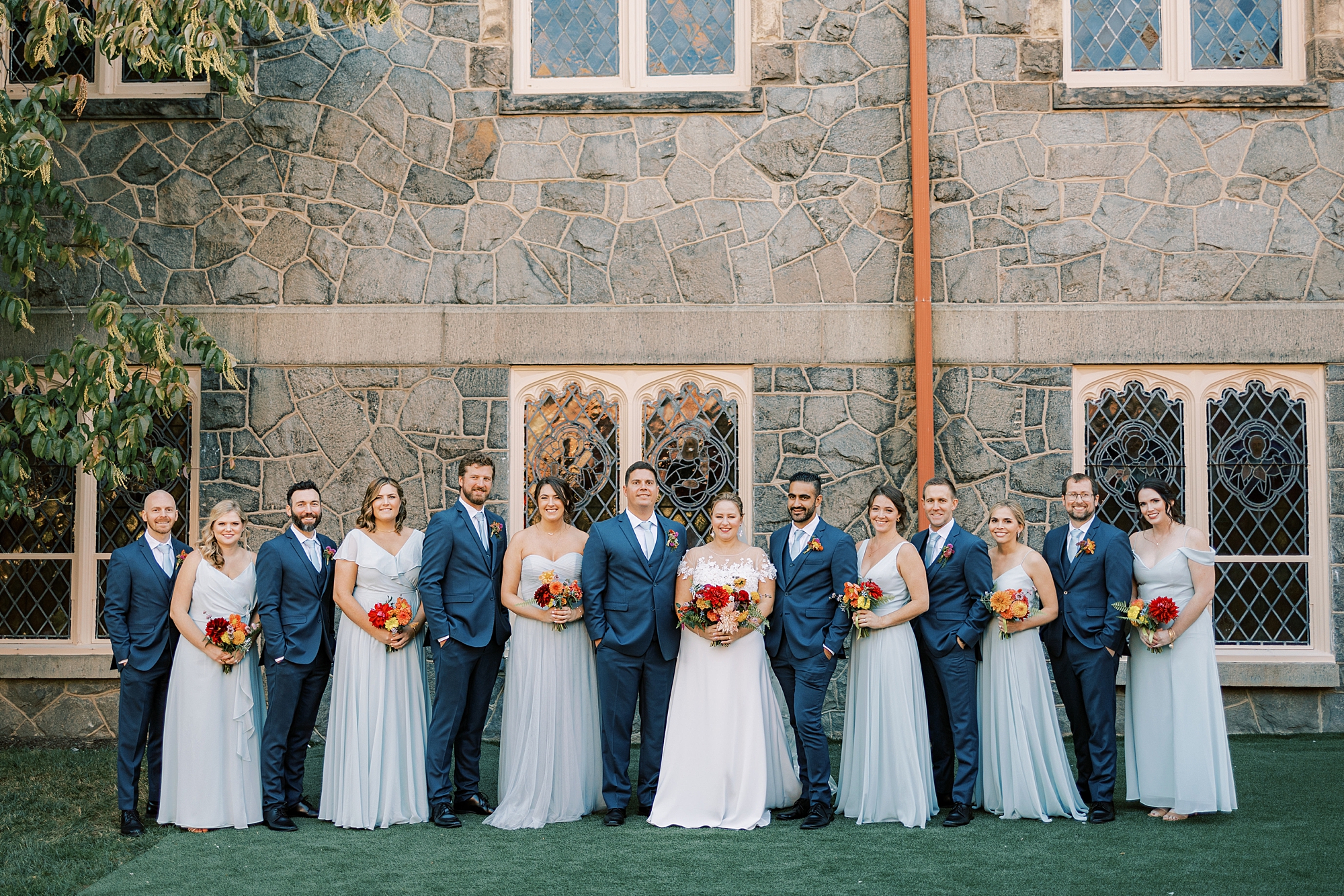 bride and groom stand with wedding party in navy suits and light blue dresses 