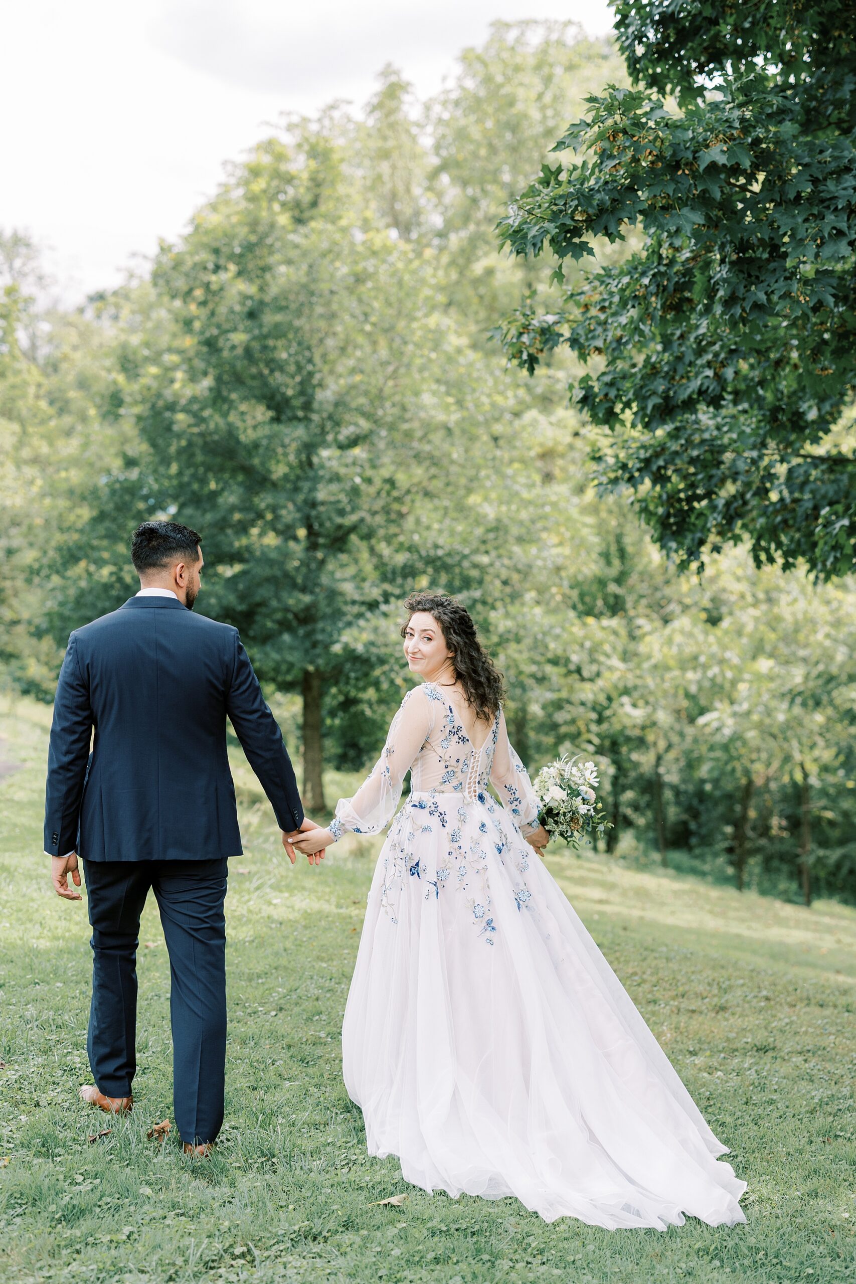 bride and groom hold hands walking on lawn at John James Audubon Center