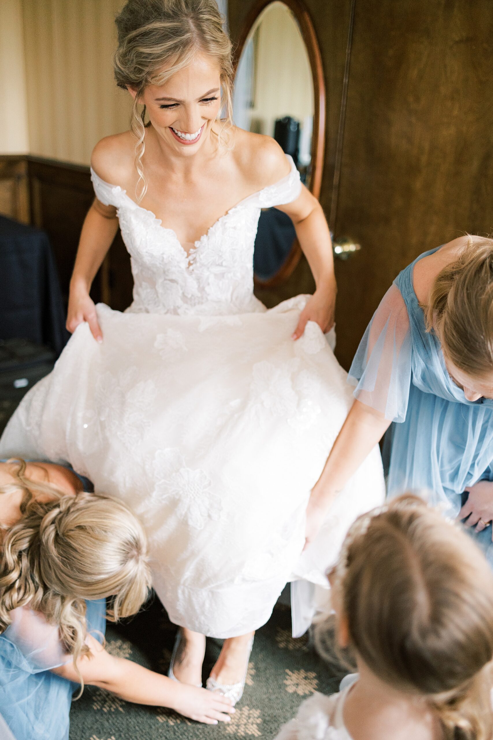 bridesmaids in blue dresses help bride into gown 