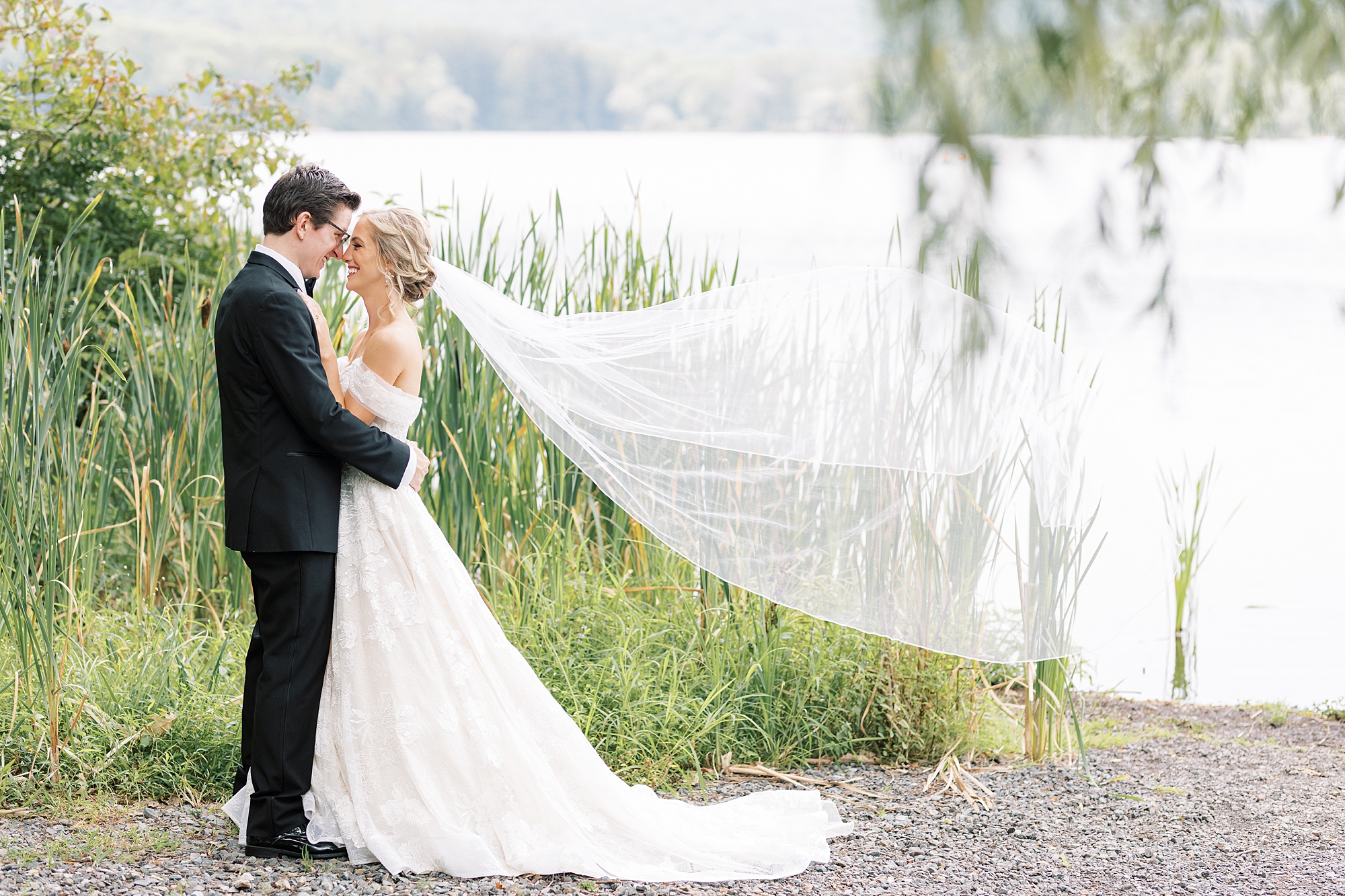newlyweds lean together touching noses while bride's veil floats behind them 
