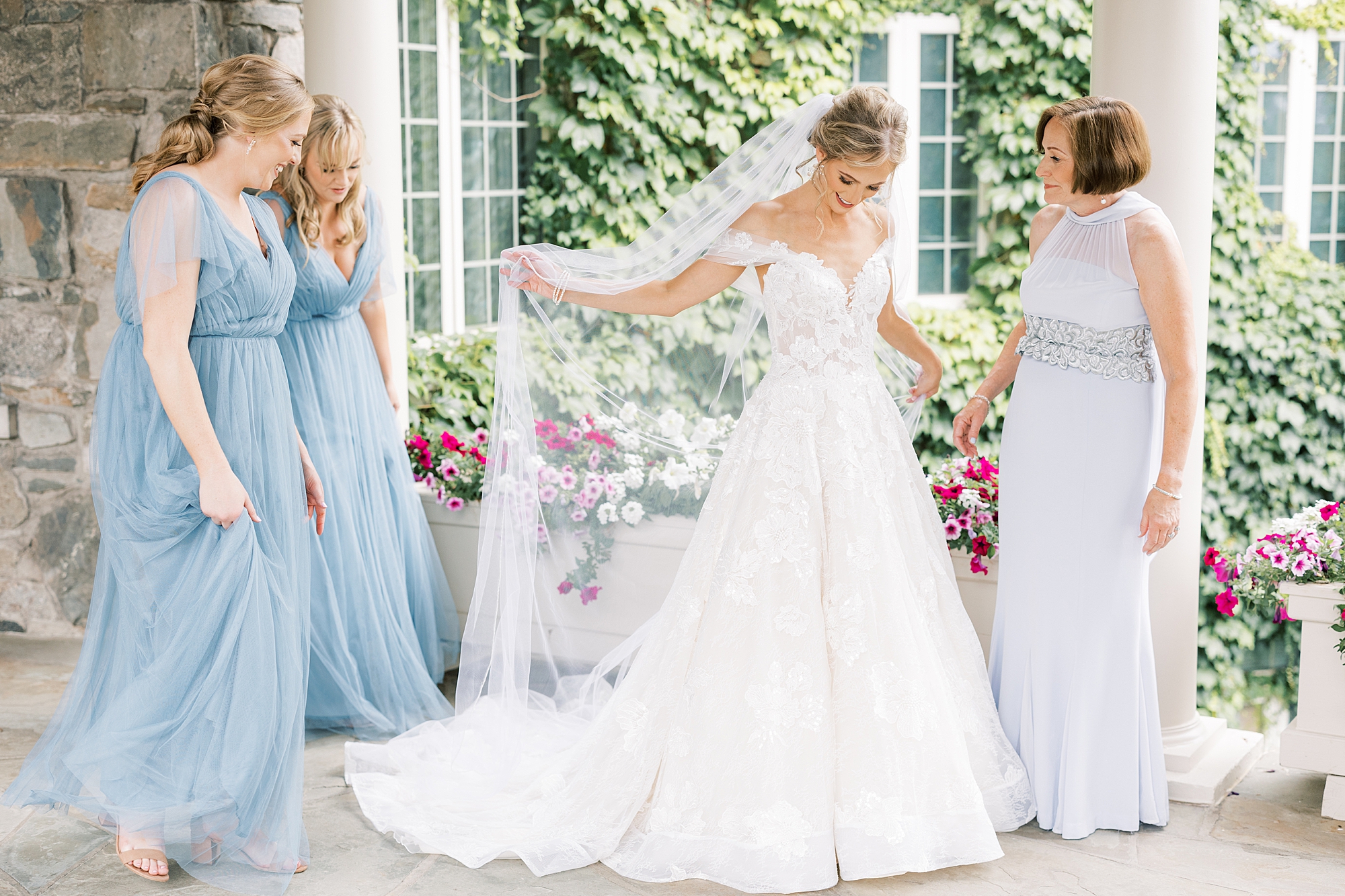 bride shows off wedding dress and veil to mother and bridesmaids 