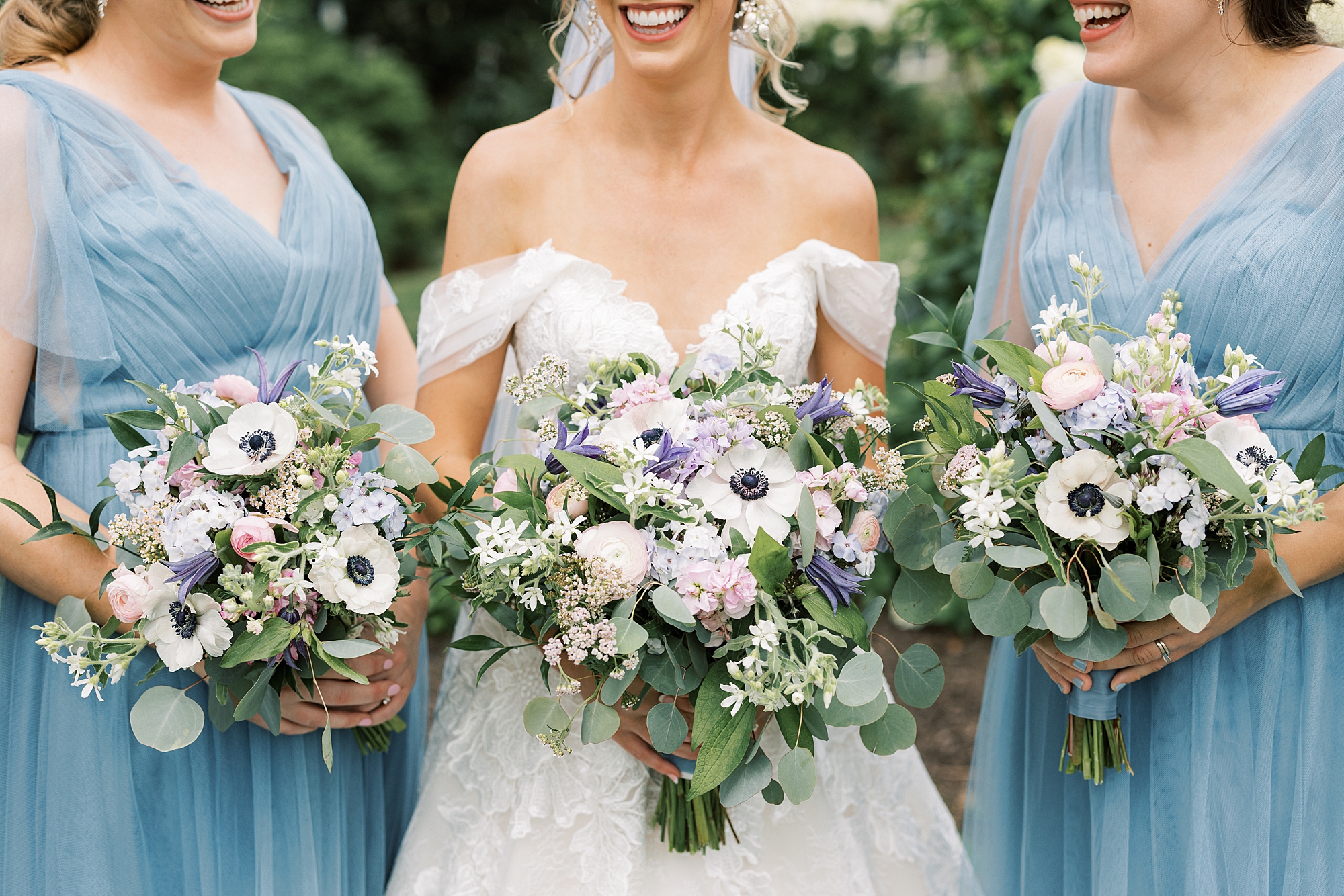 bride stands with bridesmaids in blue dresses holding pink and purple flowers 