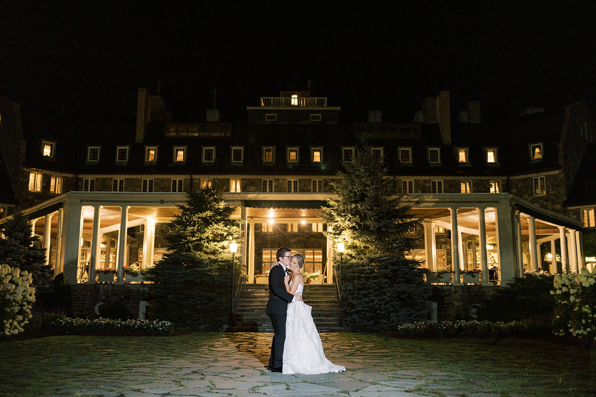 bride and groom hug in front of Skytop Lodge lit up at night