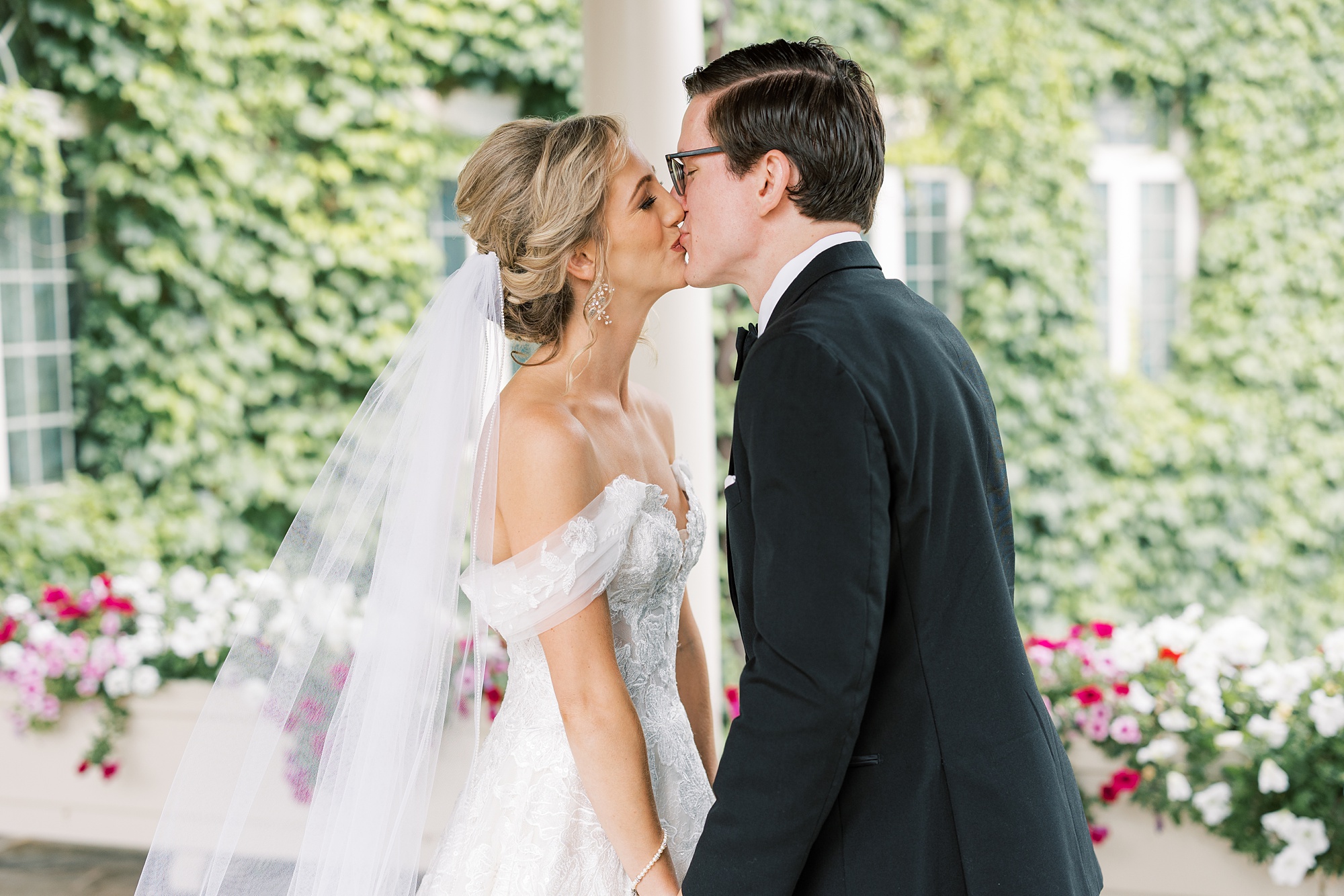 bride and groom kiss in front of green bushes 