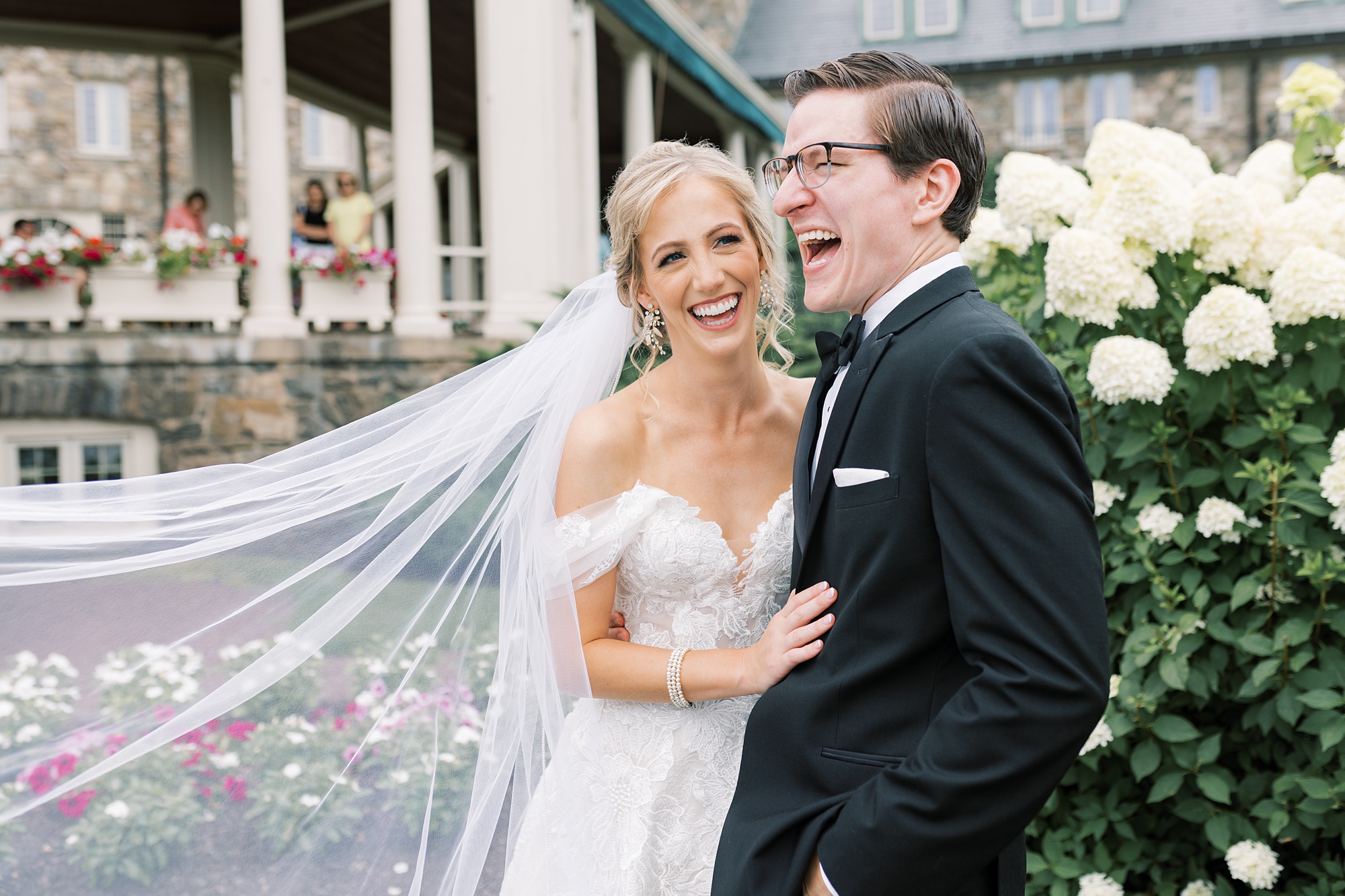 bride and groom laugh  in front of white hydrangeas at Skytop Lodge