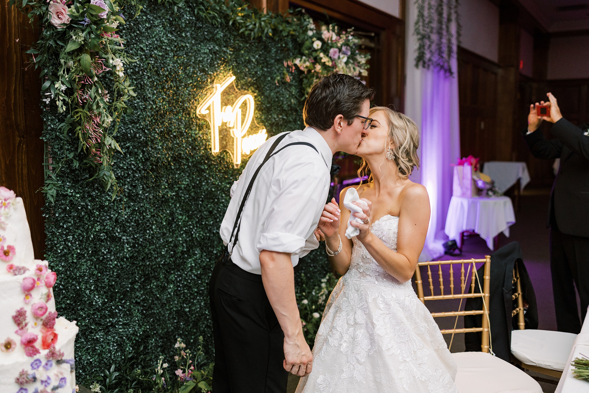 bride and groom kiss in front of greenery wall 