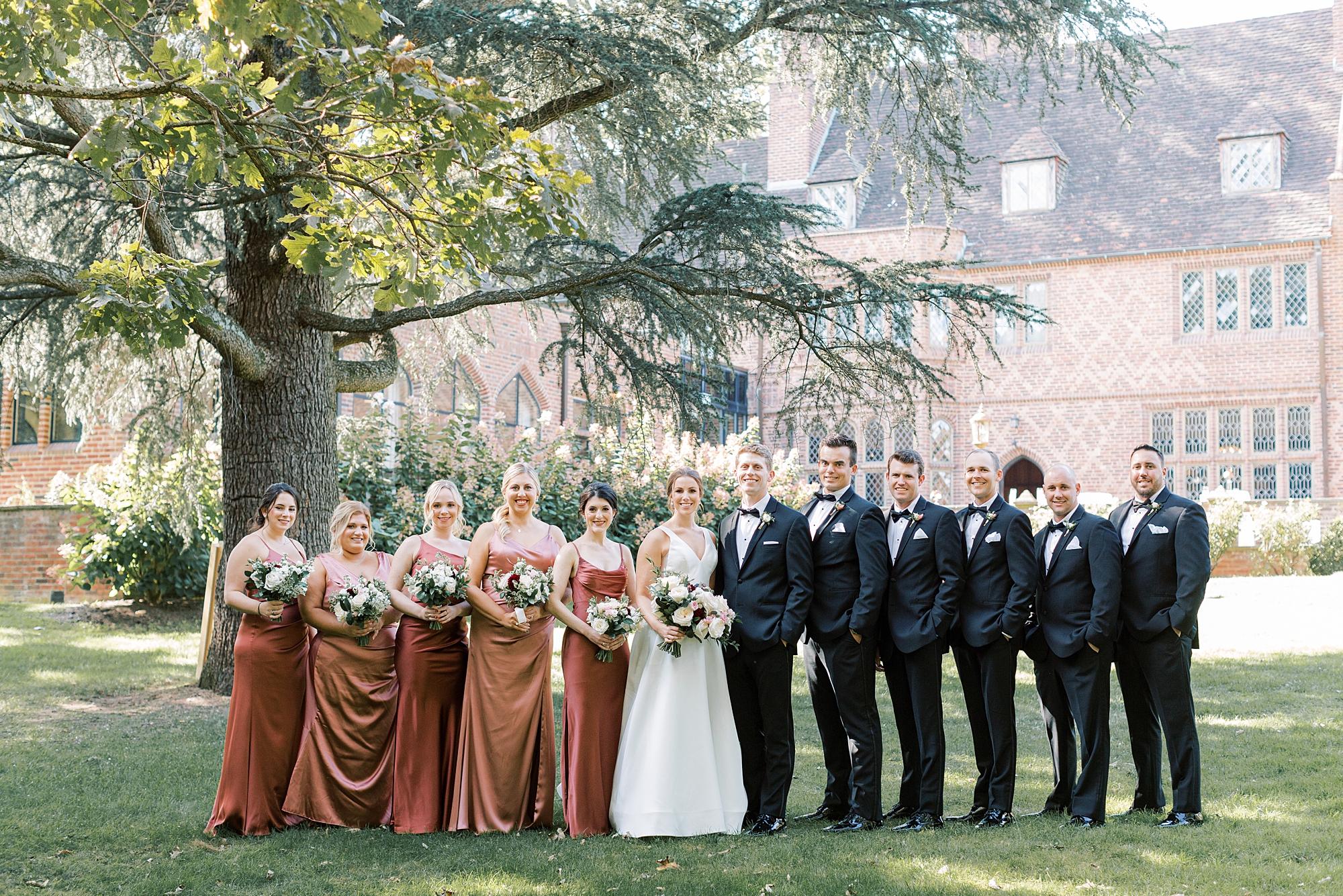 bride and groom walk with wedding party in black suits and burnt orange gowns at Aldie Mansion