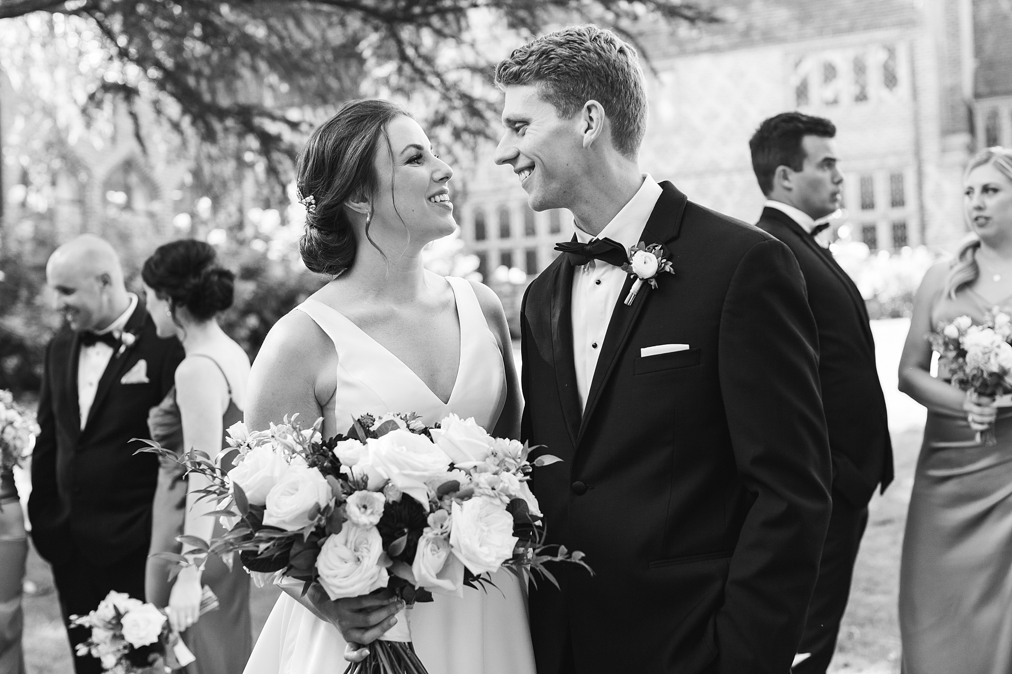 black and white photo of bride and groom smiling in front of wedding party