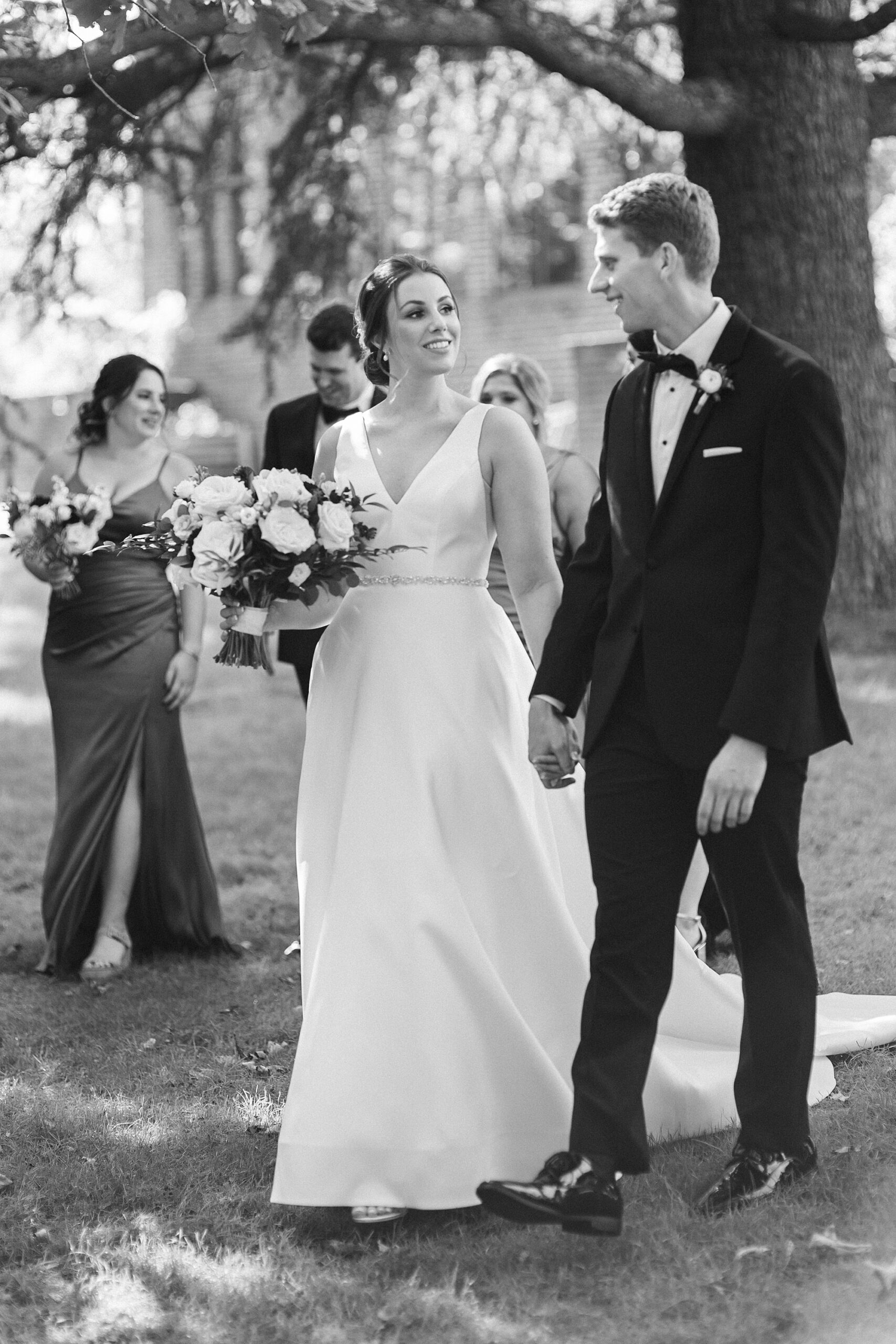 black and white photo of bride and groom walking on lawn at Aldie Mansion with wedding party 
