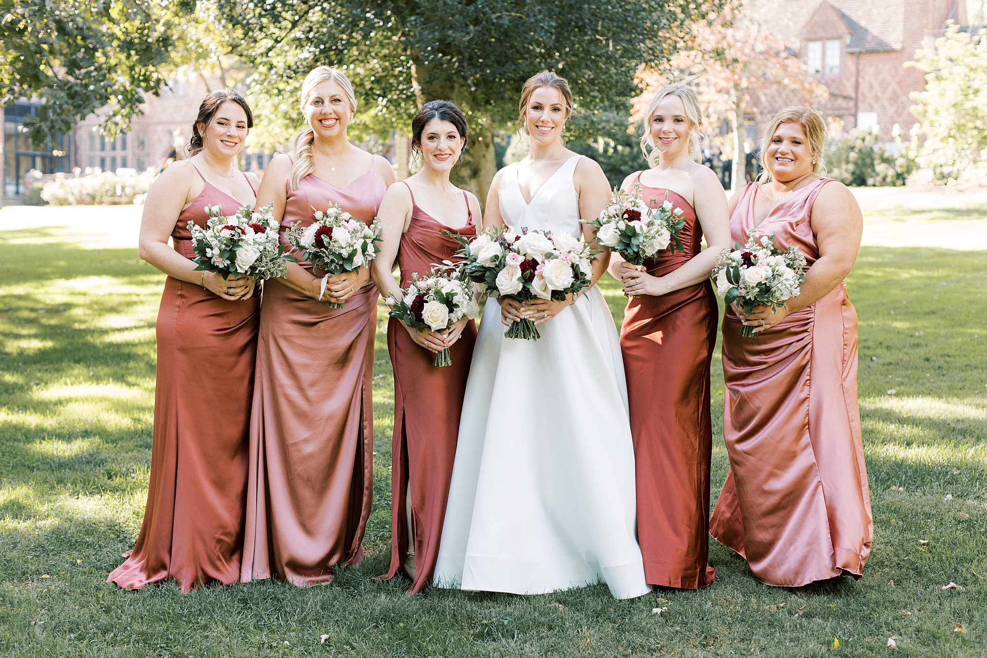 bride stands with bridesmaids in mismatched pink and burnt orange gowns 