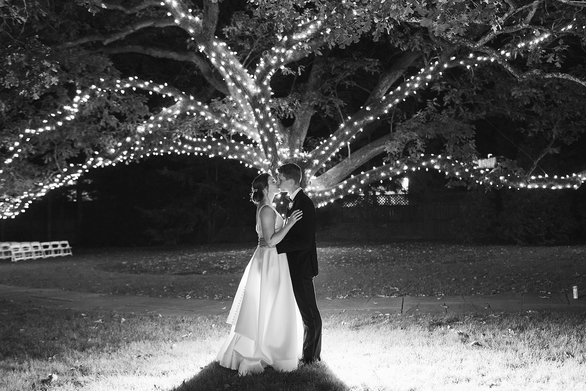 bride and groom kiss under tree with sparkling lights 
