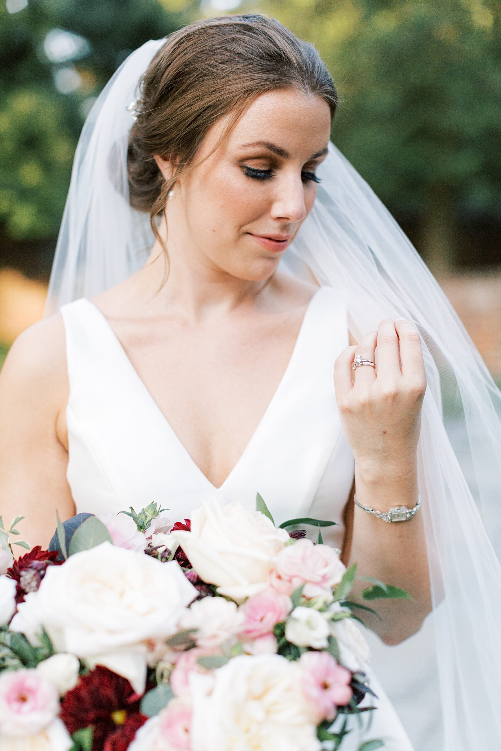 bride stands pulling veil around shoulders holding bouquet of pink, white, and red flowers