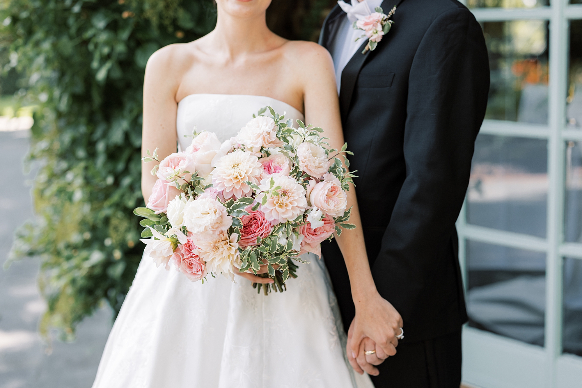 bride and groom hold hands while bride holds bouquet of pink flowers 