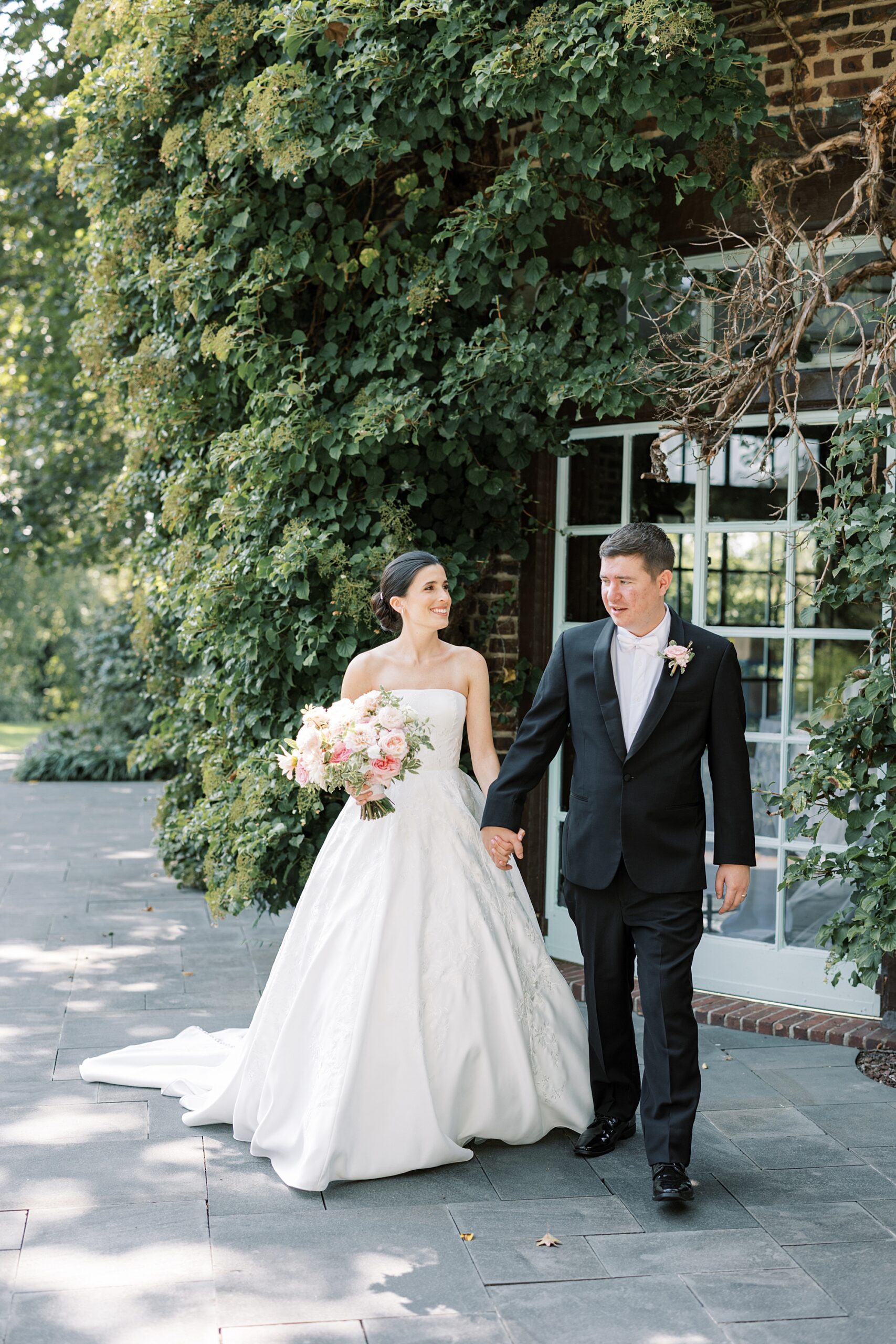 newlyweds hold hands walking together near greenhouse at Greenville Country Club