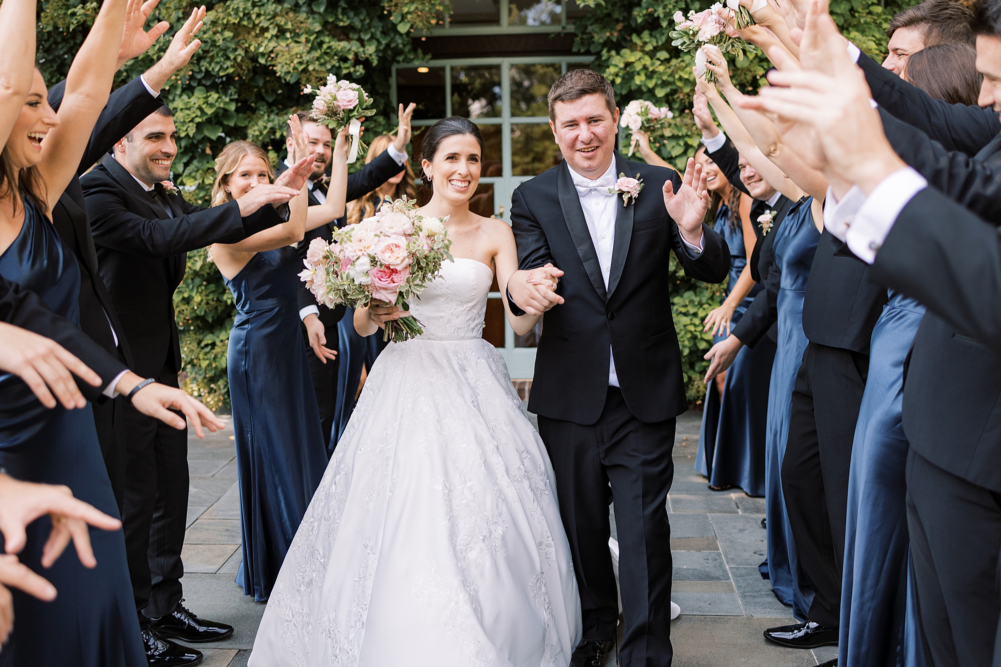 newlyweds smile walking through wedding party cheering with their arms in the air 