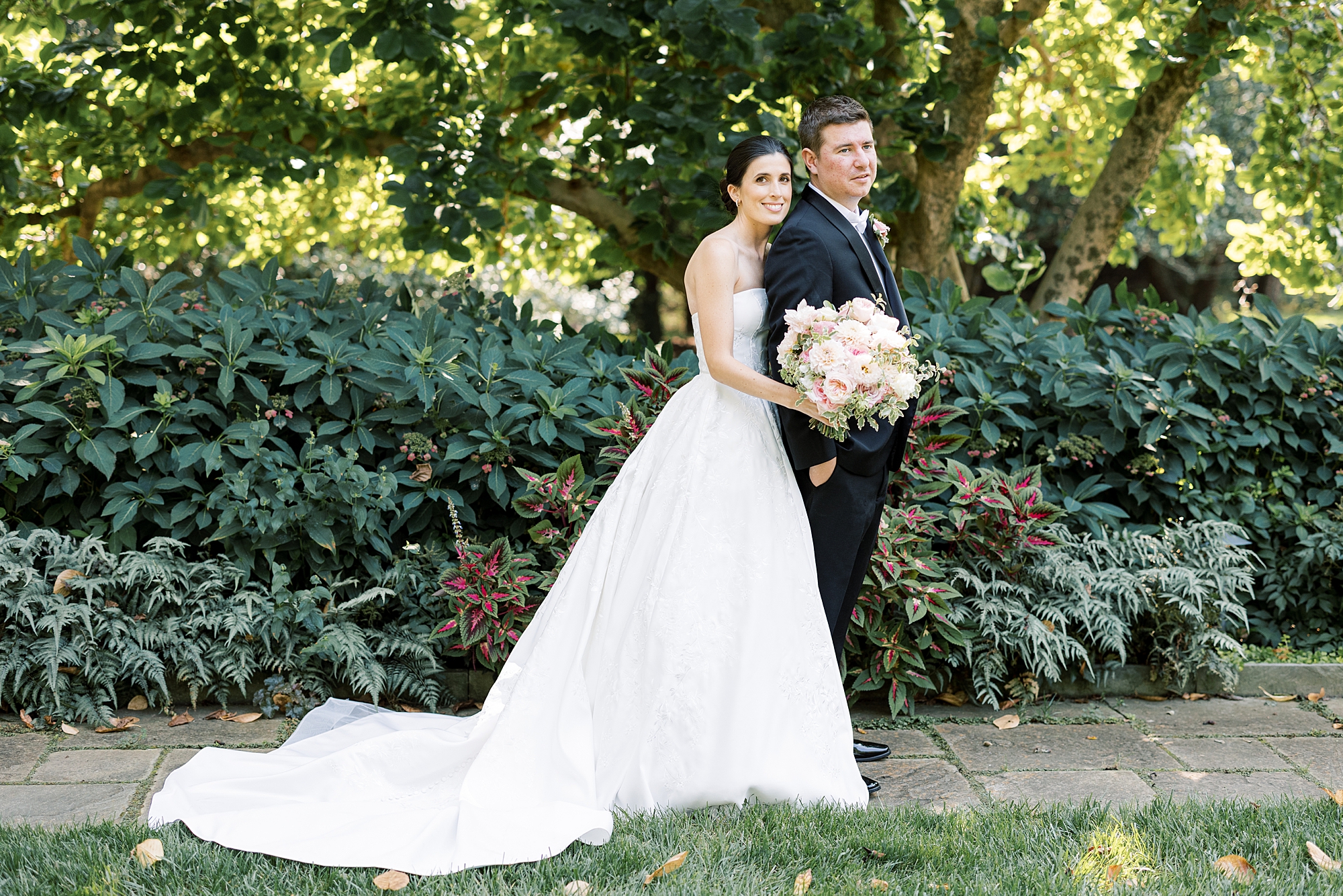 bride leans into groom's back standing by bushes at Greenville Country Club